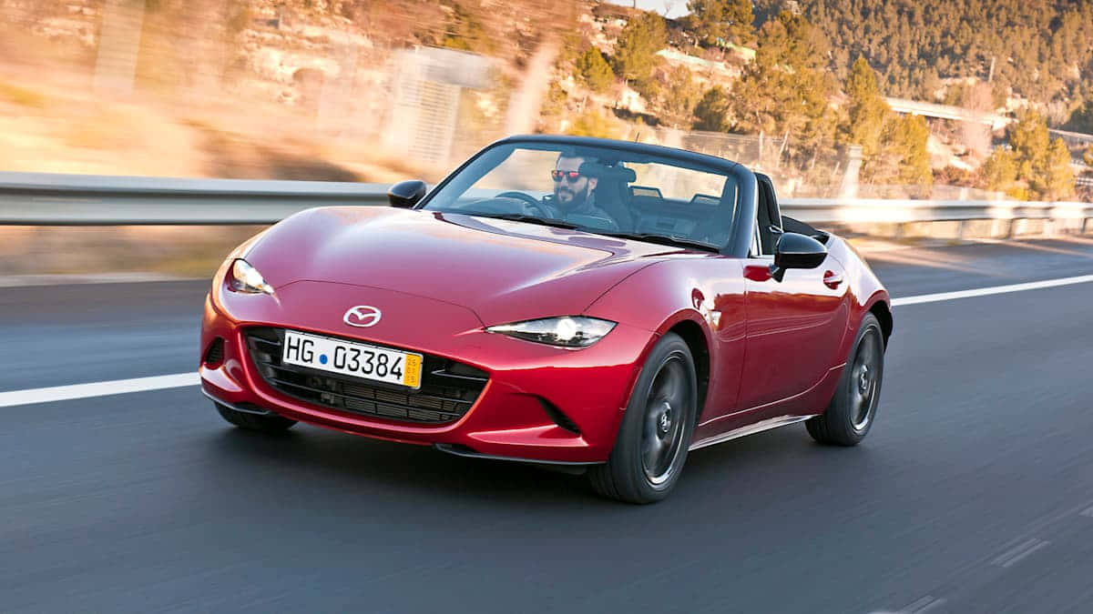 Fiat 124 Spider 桌布 壁紙 — 一輛充滿活力的紅色Mazda MX-5 Miata開篷跑車在蜿蜒的山路上奔馳，背景模糊。