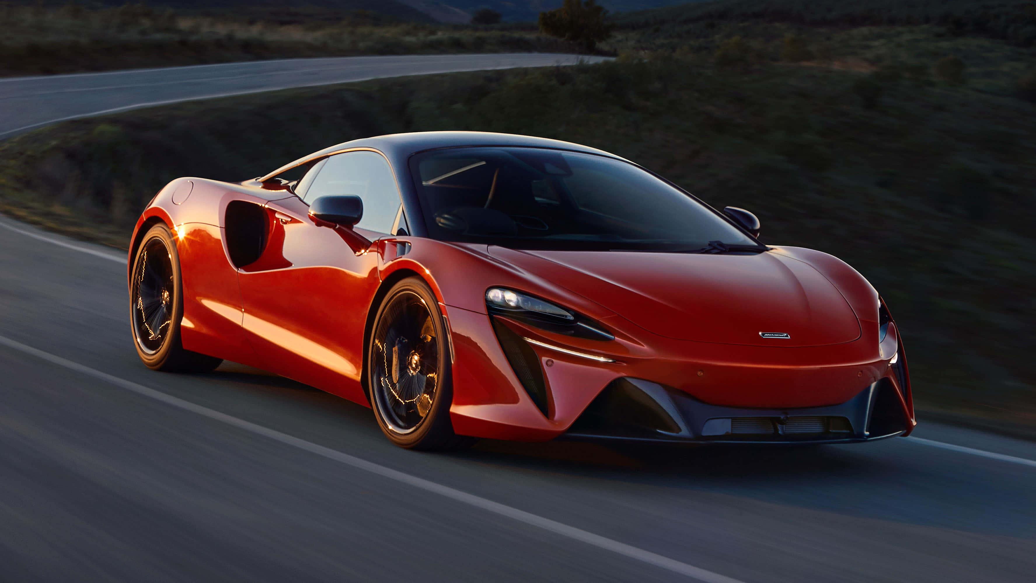 麥拿侖 桌布 壁紙 — 一輛充滿活力的紅色McLaren跑車在日落時分沿著蜿蜒的山路疾馳，呈現模糊的動態效果。