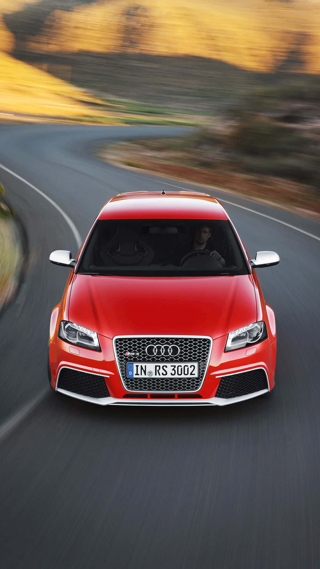 Audi Rs3 桌布 壁紙 — 一輛充滿活力的紅色奧迪RS3在蜿蜒的道路上疾馳，金色的山丘在背景中模糊。