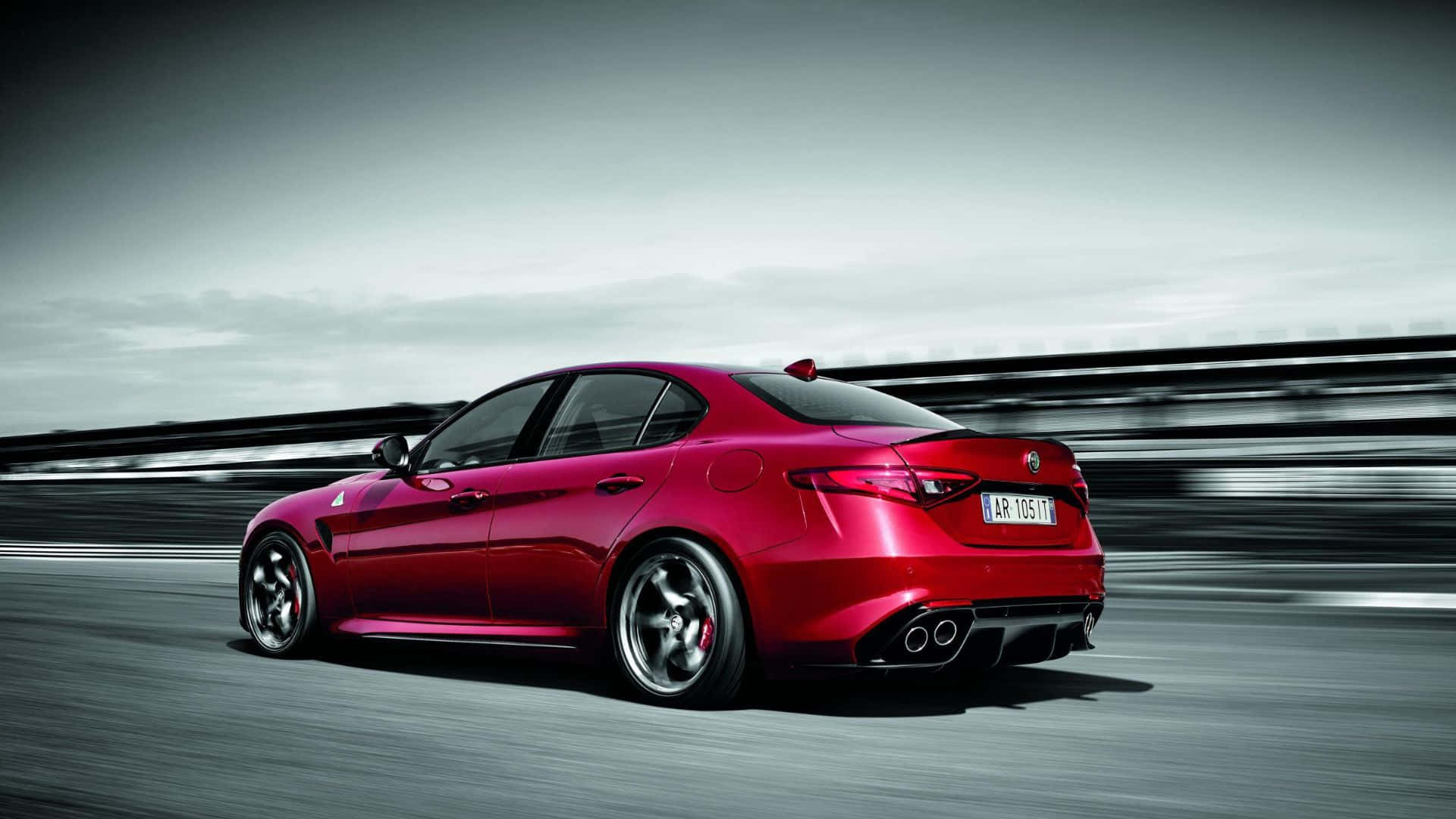 Alfa Romeo Giulia 桌布 壁紙 — 一輛充滿活力的紅色愛快羅密歐房車在陰天下的模糊賽道上疾馳。