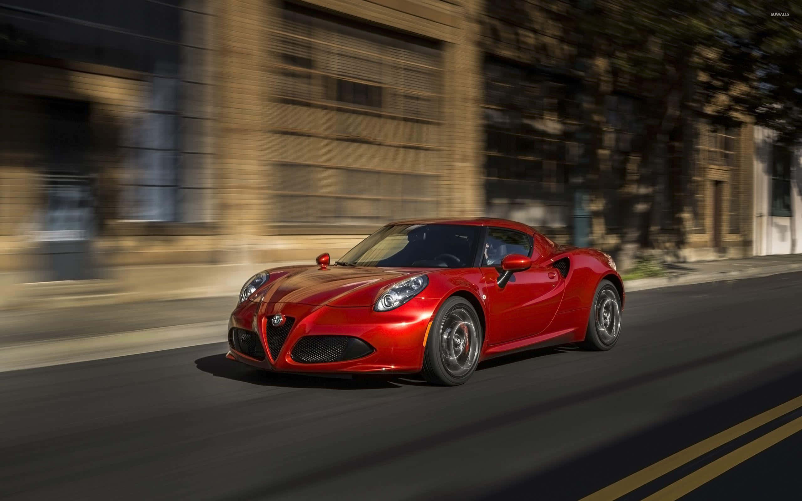 Alfa Romeo 4c 桌布 壁紙 — 一輛充滿活力的紅色愛快羅密歐跑車在陽光明媚的城市街道上疾馳，背景建築物呈現動態模糊效果。