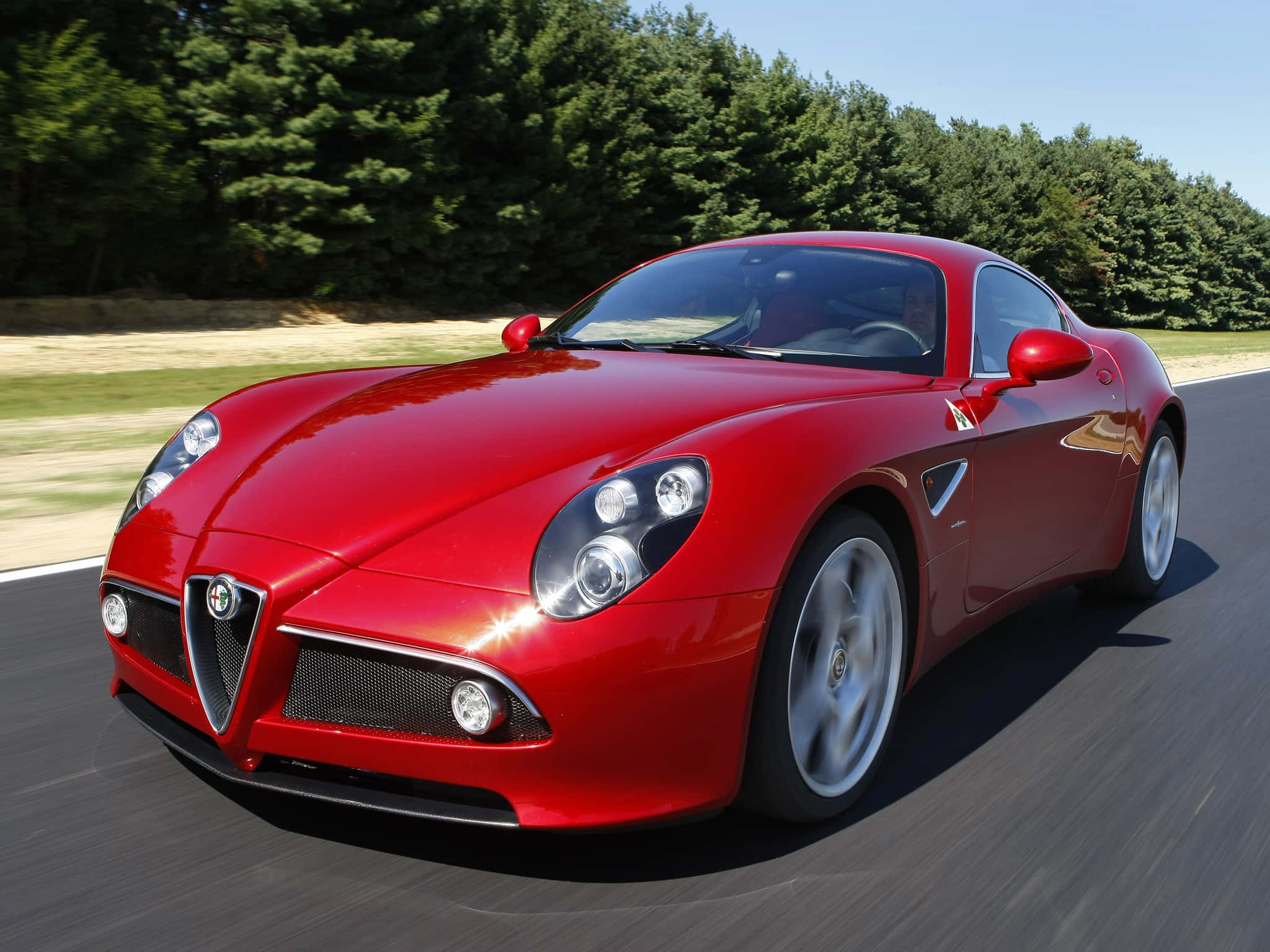 Alfa Romeo 8c Competizione 桌布 壁紙 — 一輛充滿活力的紅色愛快羅密歐跑車在陽光明媚的道路上行駛，背景是茂密的綠樹。
