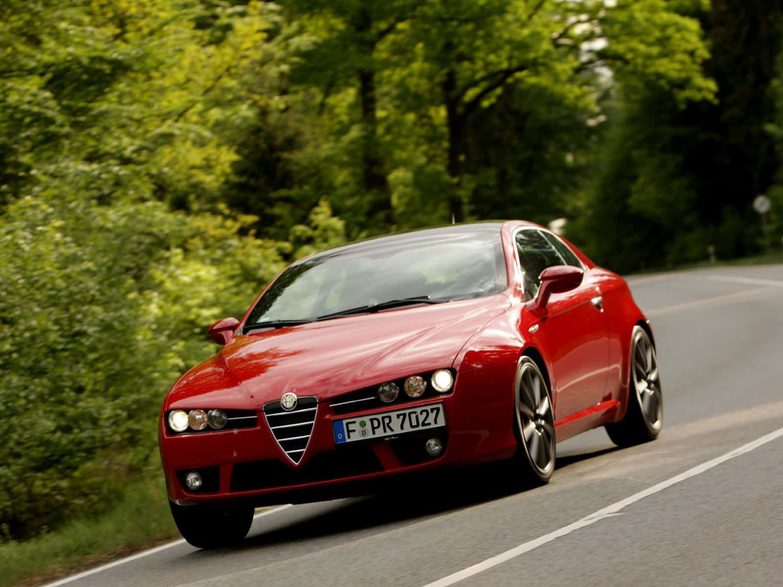Alfa Romeo Brera 桌布 壁紙 — 一輛充滿活力的紅色愛快羅密歐跑車在蜿蜒的林間道路上飛馳，周圍是茂密的綠樹。