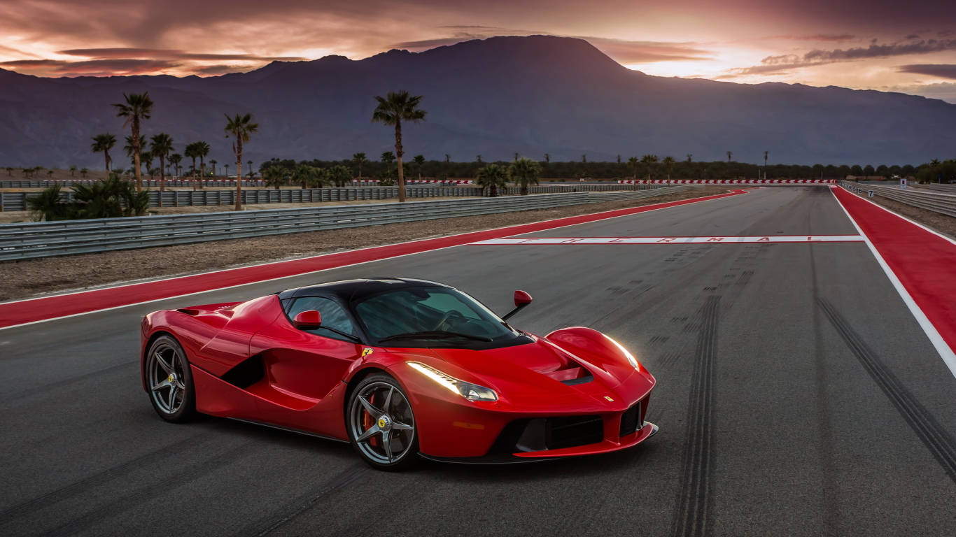 Sports Car 桌布 壁紙 — 一輛充滿活力的紅色法拉利 LaFerrari 在日落時分沿著賽道飛馳，背景有棕櫚樹和山脈。