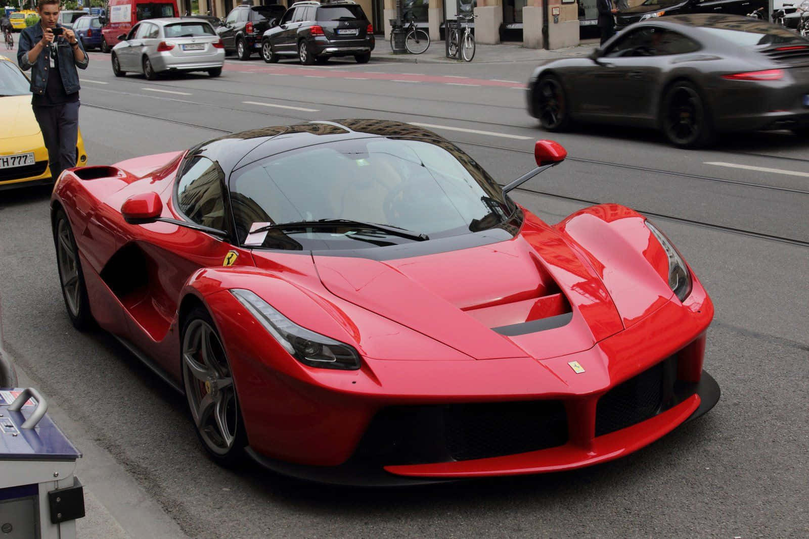 Ferrari Laferrari 桌布 壁紙 — 一輛充滿活力的紅色法拉利LaFerrari跑車停泊在繁忙的城市街道上，背景有模糊的交通和一位攝影師。