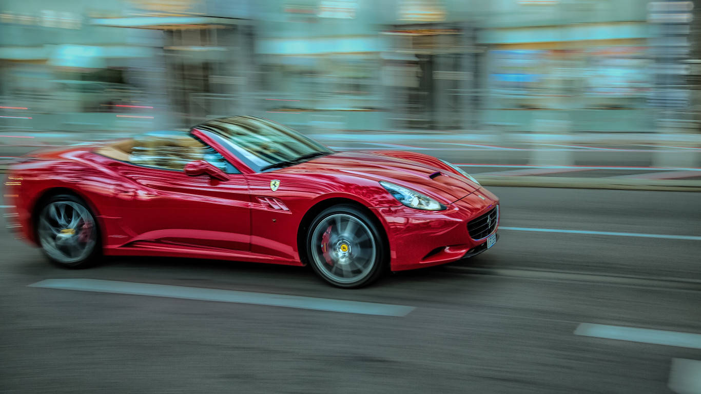 Sports Car 桌布 壁紙 — 一輛充滿活力的紅色法拉利敞篷車在模糊的城市街道上飛馳，捕捉動感與奢華。