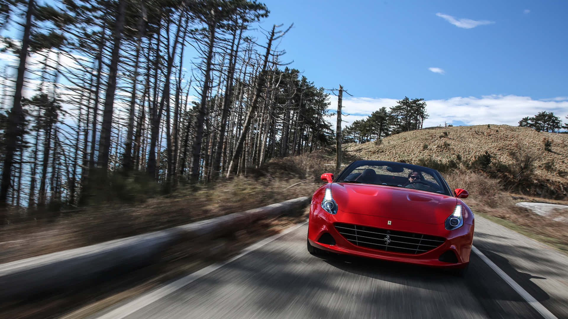 Ferrari California T 桌布 壁紙 — 一輛充滿活力的紅色法拉利跑車在晴朗的藍天下沿著蜿蜒的林間道路飛馳。