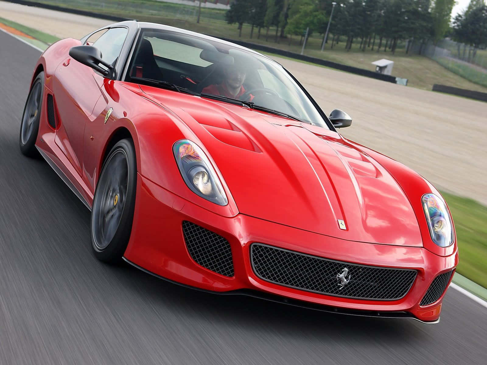 Ferrari 599 Gtb Fiorano 桌布 壁紙 — 一輛充滿活力的紅色法拉利跑車在賽道上疾馳，背景有模糊的動感和綠樹。