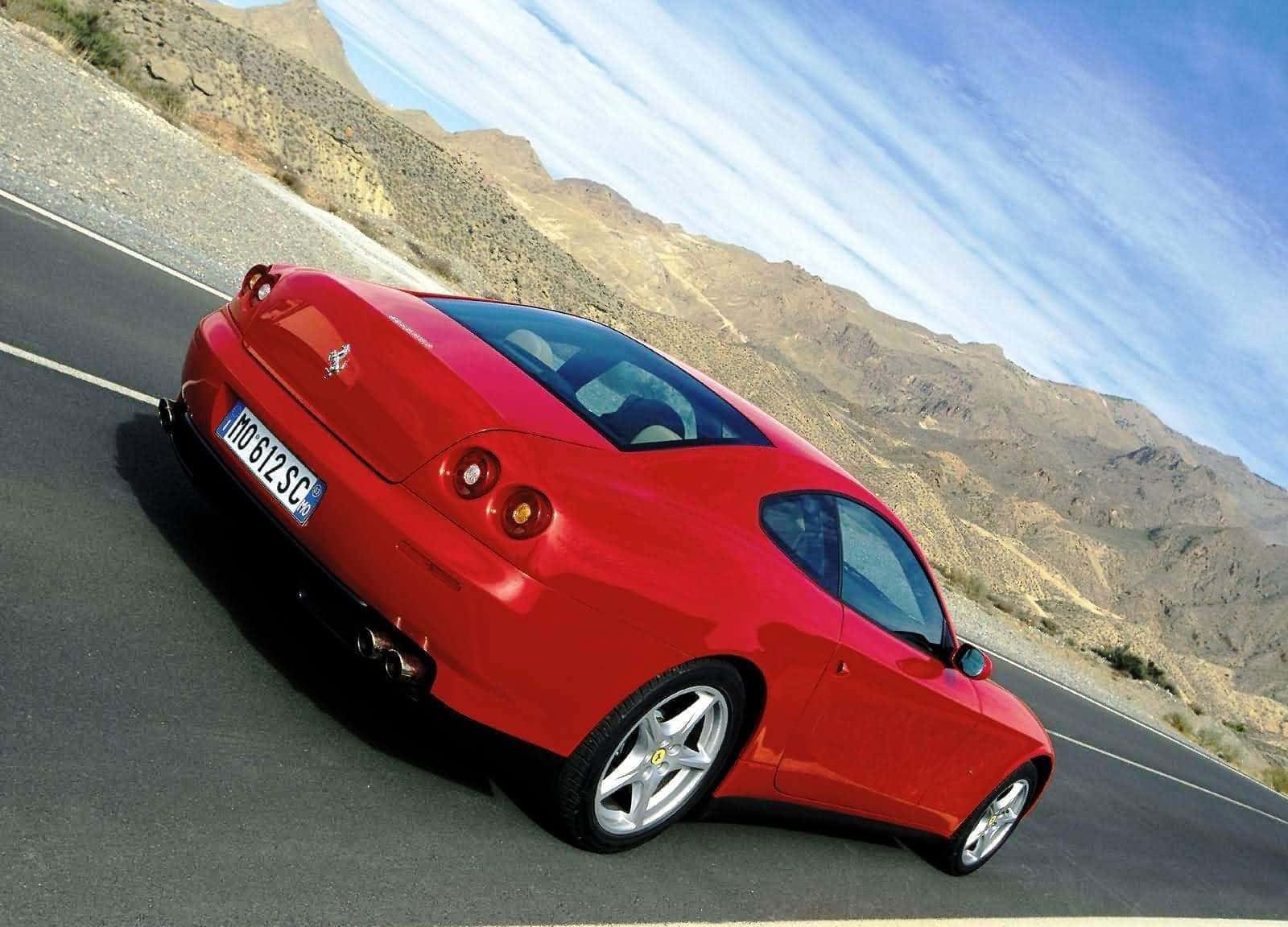 Ferrari 612 Scaglietti 桌布 壁紙 — 一輛充滿活力的紅色法拉利跑車沿著蜿蜒的山路行駛，天空湛藍，白雲輕飄。