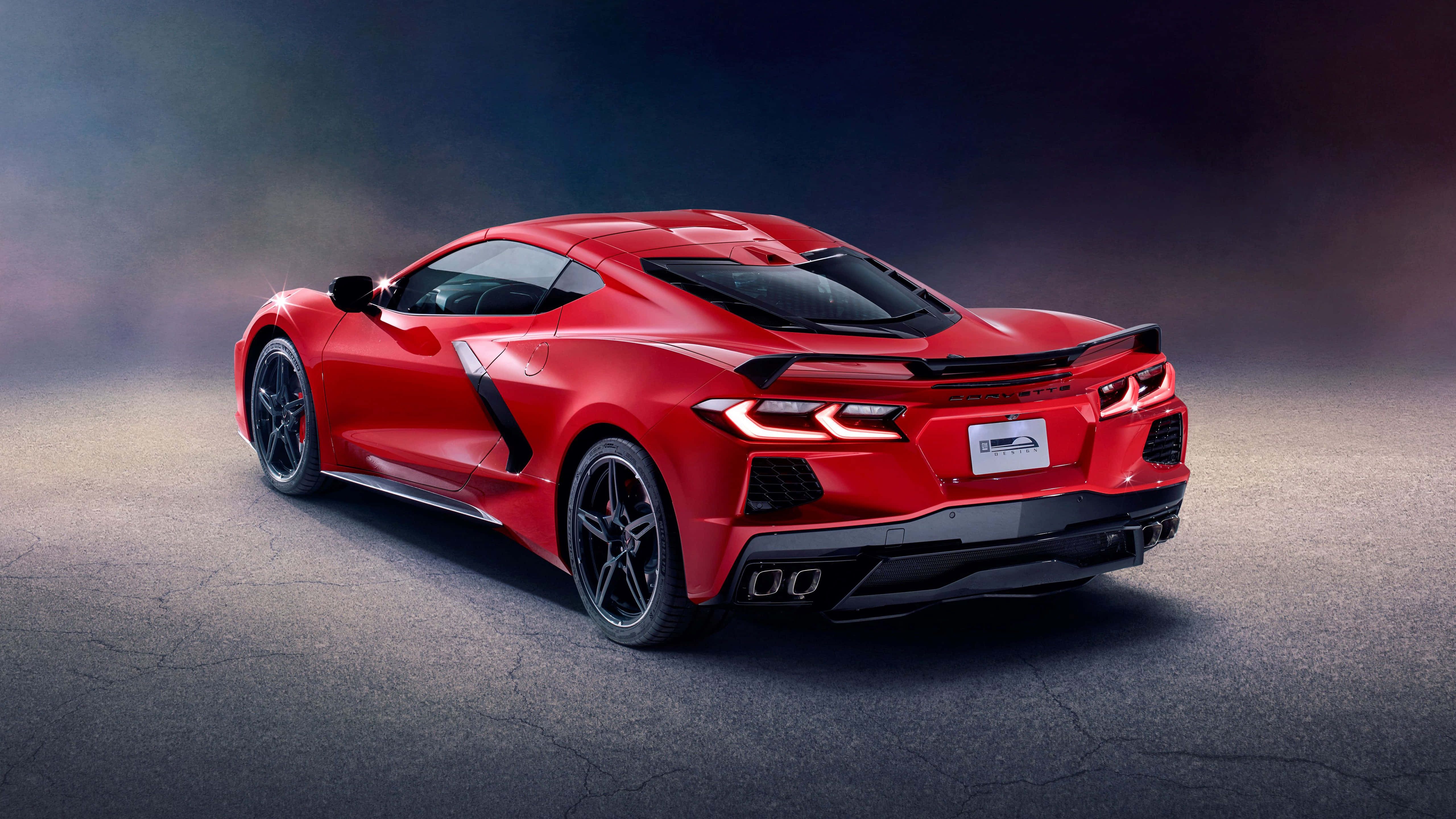 Chevrolet Corvette Stingray 桌布 壁紙 — 一輛充滿活力的紅色跑車，帶有發光的尾燈，在戲劇性的工作室燈光下立於破裂的瀝青路面上。