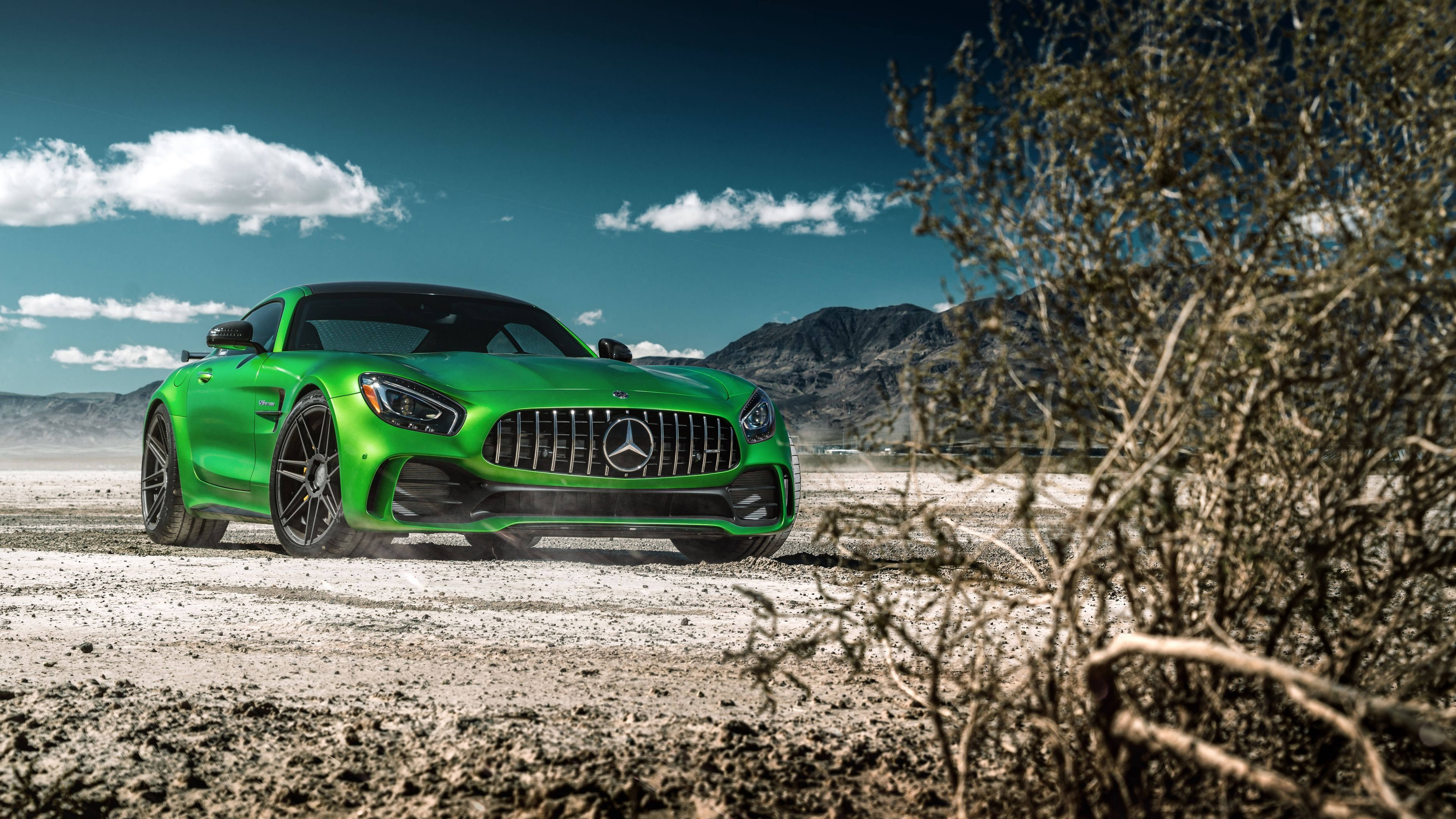 HD mercedes 桌布 壁紙 — 一輛充滿活力的綠色 Mercedes-AMG GT 跑車，在晴朗藍天和零星白雲下，疾馳過塵土飛揚的沙漠景觀。