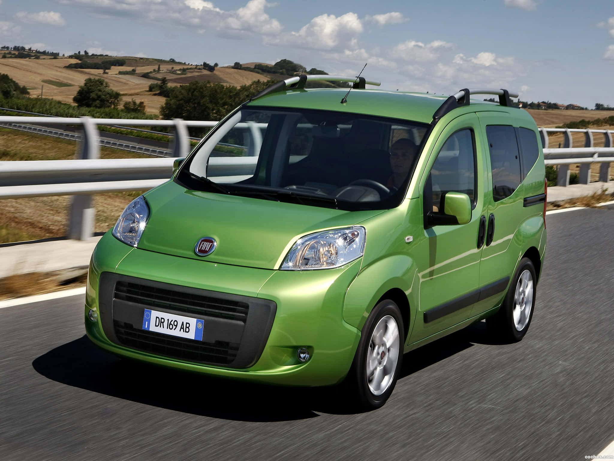 Fiat Fiorino 桌布 壁紙 — 一輛充滿活力的綠色Fiat Panda客貨車在陽光明媚的鄉村高速公路上行駛，背景是起伏的丘陵和散落的樹木。
