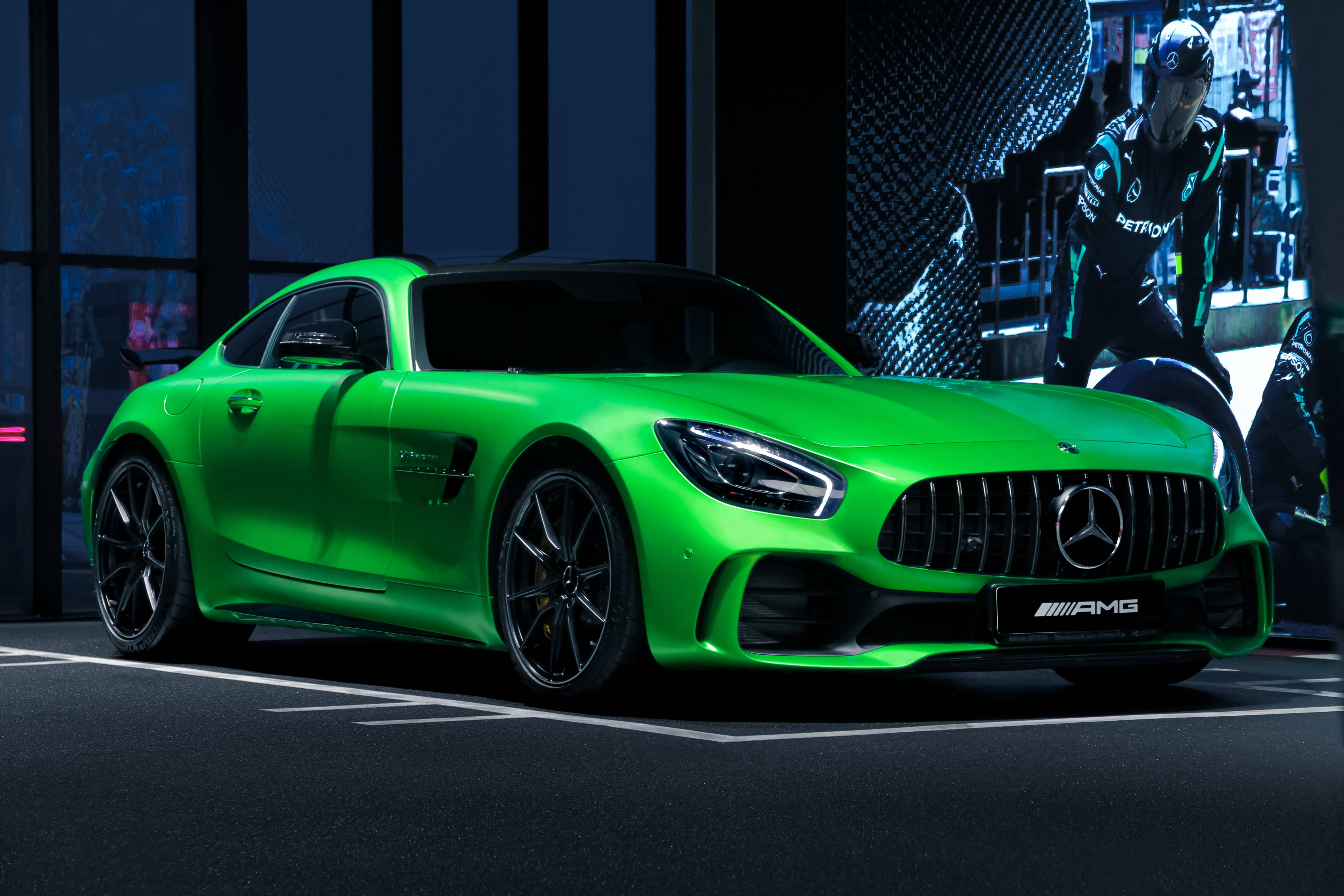 Mercedes 桌布 壁紙 — 一輛充滿活力的綠色Mercedes-AMG GT跑車在戲劇性的工作室燈光下閃閃發光，附近有一位穿著賽車裝備的技師。
