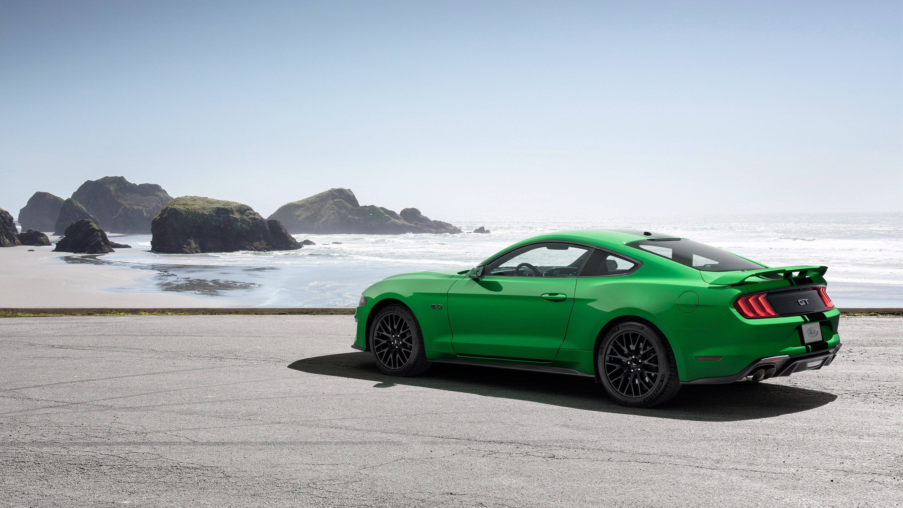 mustang HD 桌布 壁紙 — 一輛充滿活力的綠色福特野馬GT停泊在沿海道路上，背景是岩石峭壁和海洋波浪，在晴朗的藍天下。
