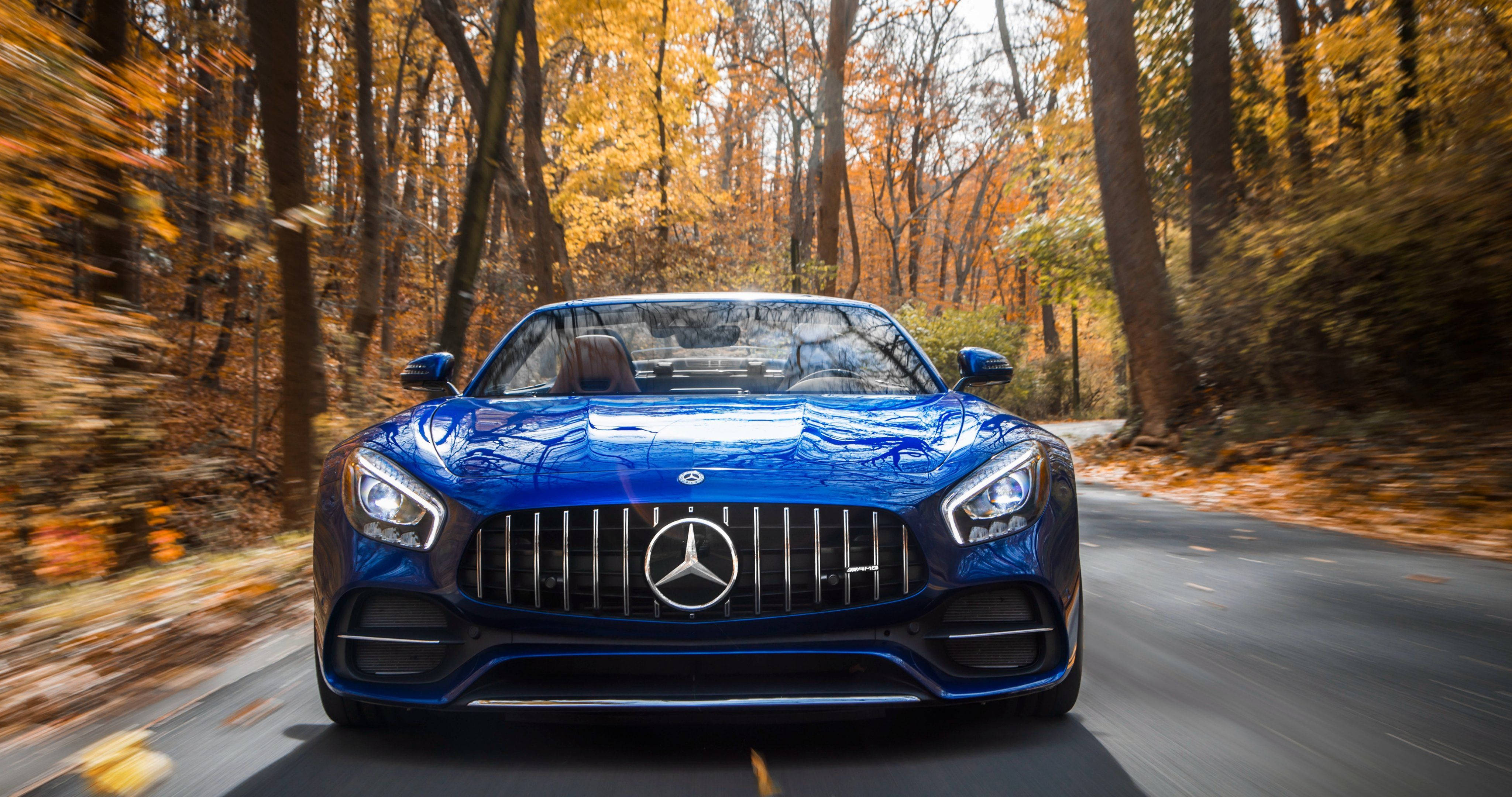 Mercedes 桌布 壁紙 — 一輛充滿活力的藍色 Mercedes-AMG GT 在金色秋葉飄落的森林中疾馳。