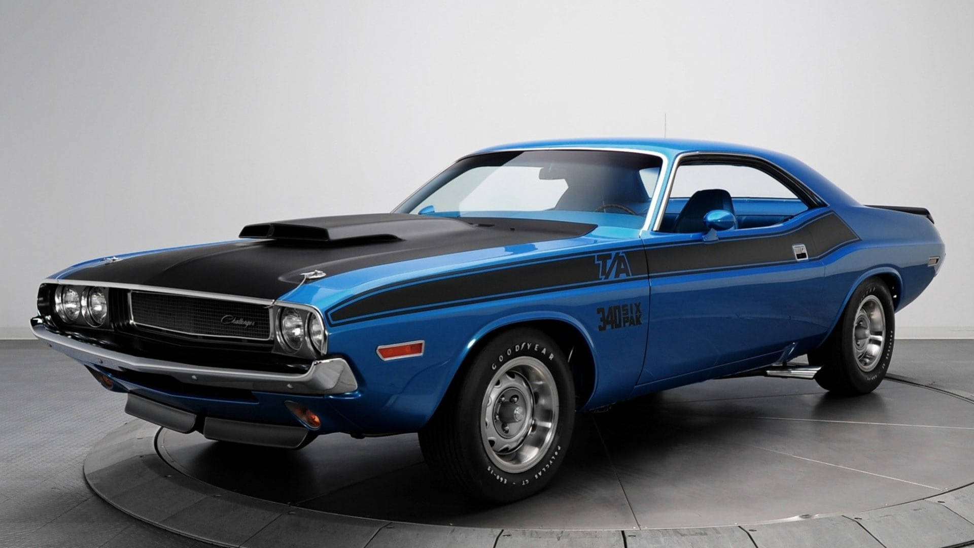 dodge challenger 桌布 壁紙 — 一輛充滿活力的藍色1970年道奇挑戰者T/A，配備黑色引擎蓋和賽車條紋，在攝影棚環境中展示。