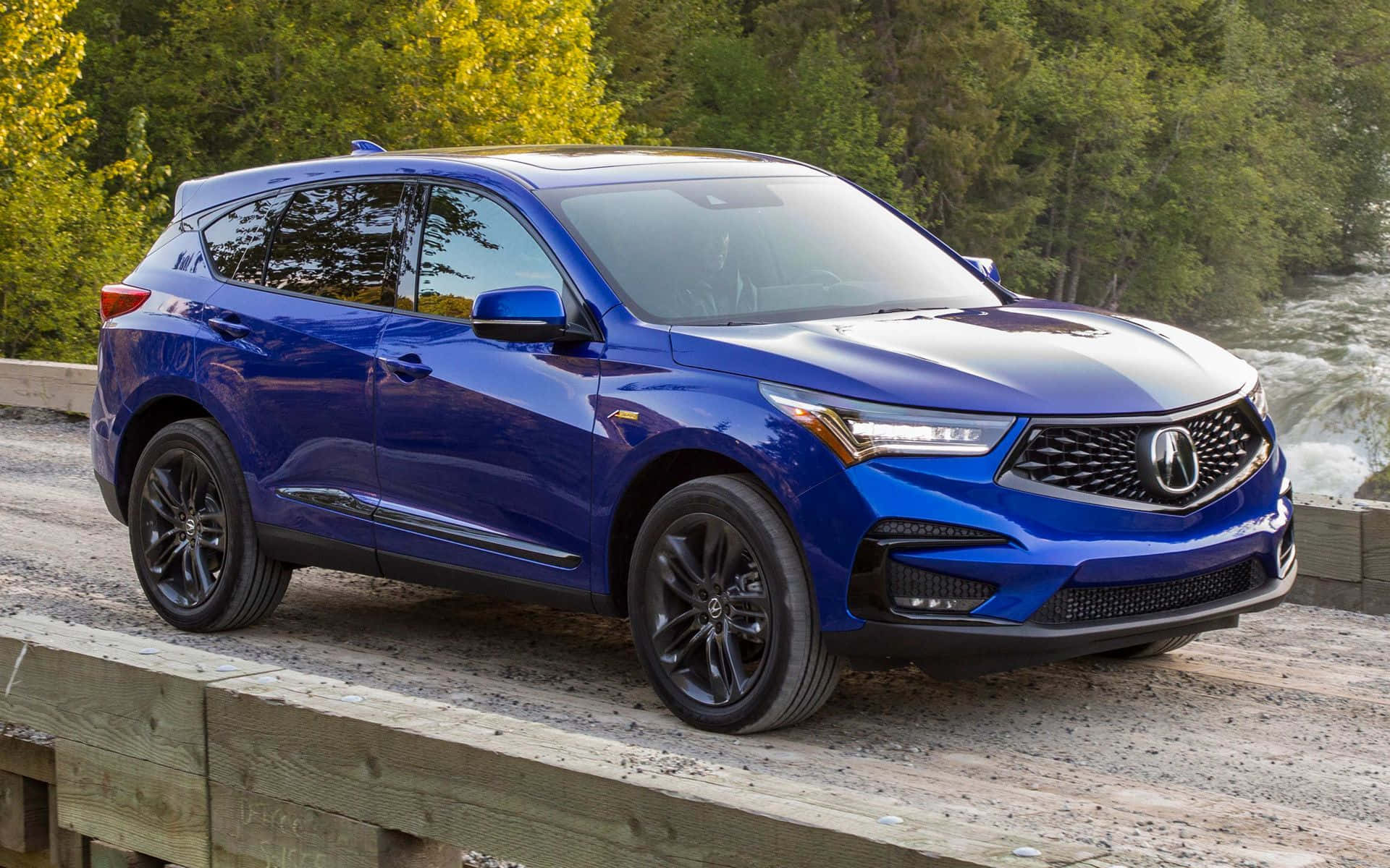 Acura Rdx 桌布 壁紙 — 一輛充滿活力的藍色Acura SUV停放在木橋上，背景是湍急的河流和秋樹。