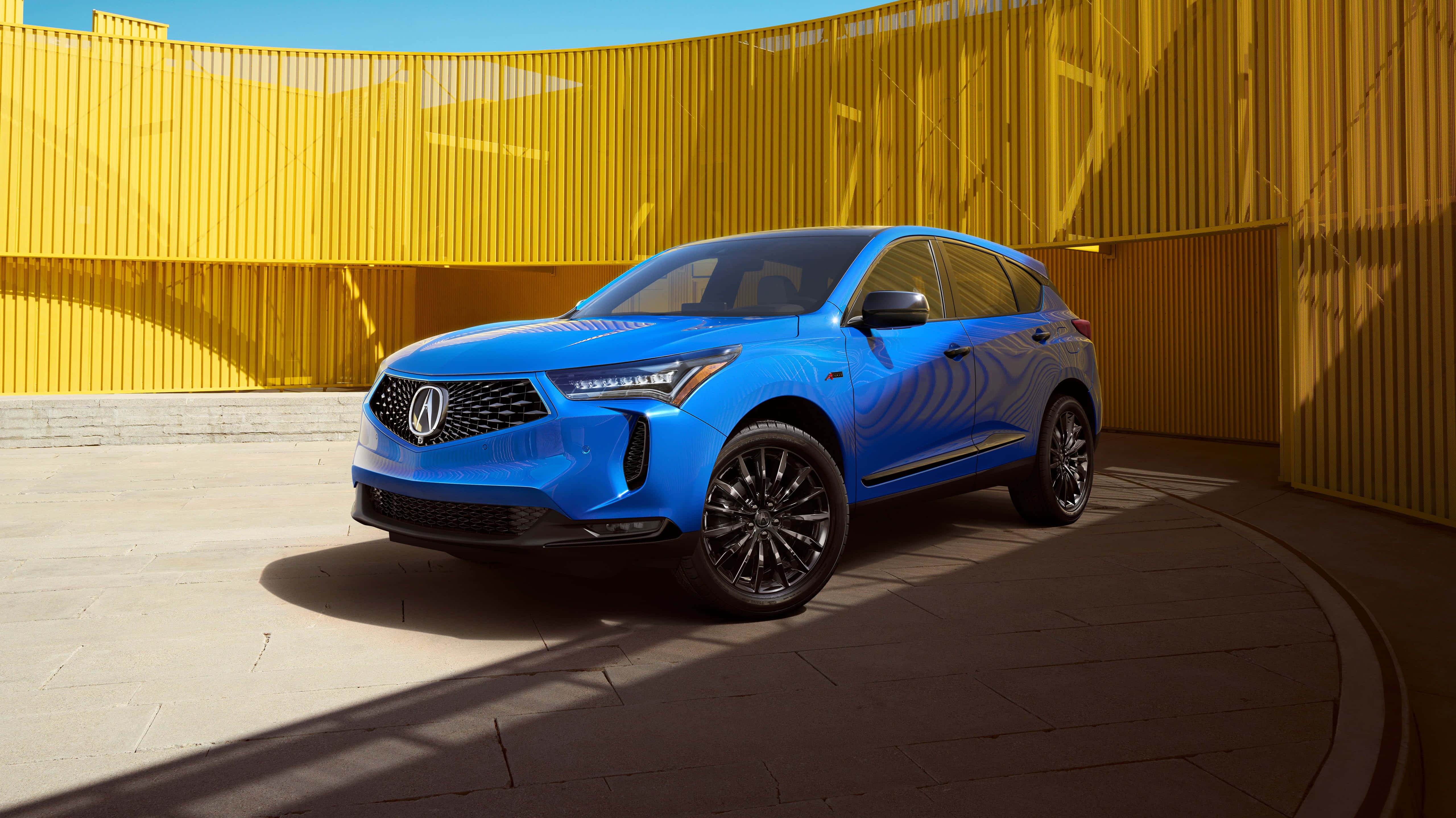 Acura Rdx 桌布 壁紙 — 一輛充滿活力的藍色Acura SUV在明亮的陽光下，以大膽的黃色波紋牆為背景，在現代都市環境中閃閃發光。