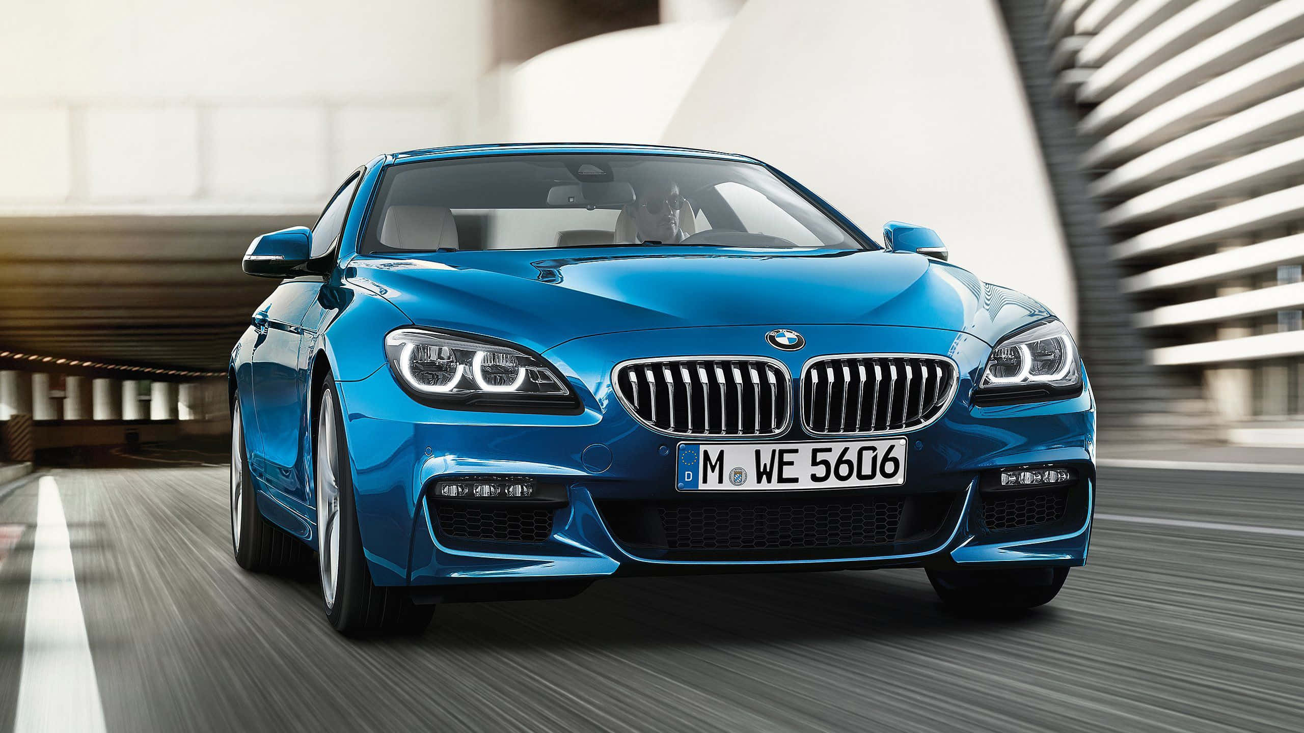 Bmw 6 Series 桌布 壁紙 — 一輛充滿活力的藍色BMW 6系轎跑車在現代城市道路上疾馳，帶有動態模糊效果和時尚的建築環境。