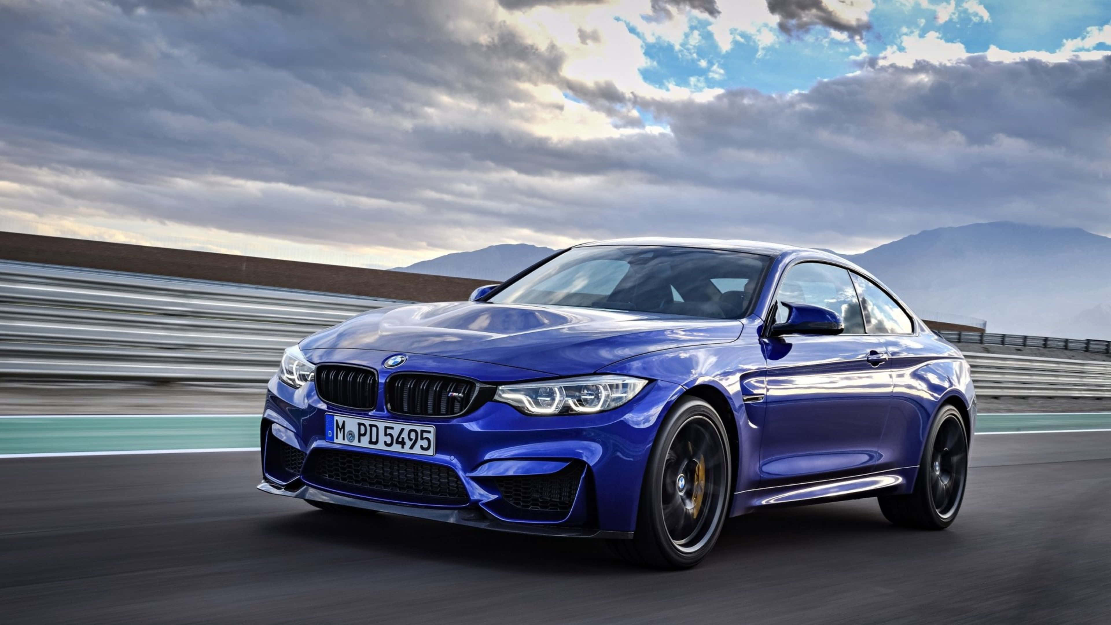 4K BMW 壁紙 桌布 壁紙 — 一輛充滿活力的藍色BMW M4 Coupe在戲劇性的多雲天空下，以模糊的動態沿著賽道飛馳。