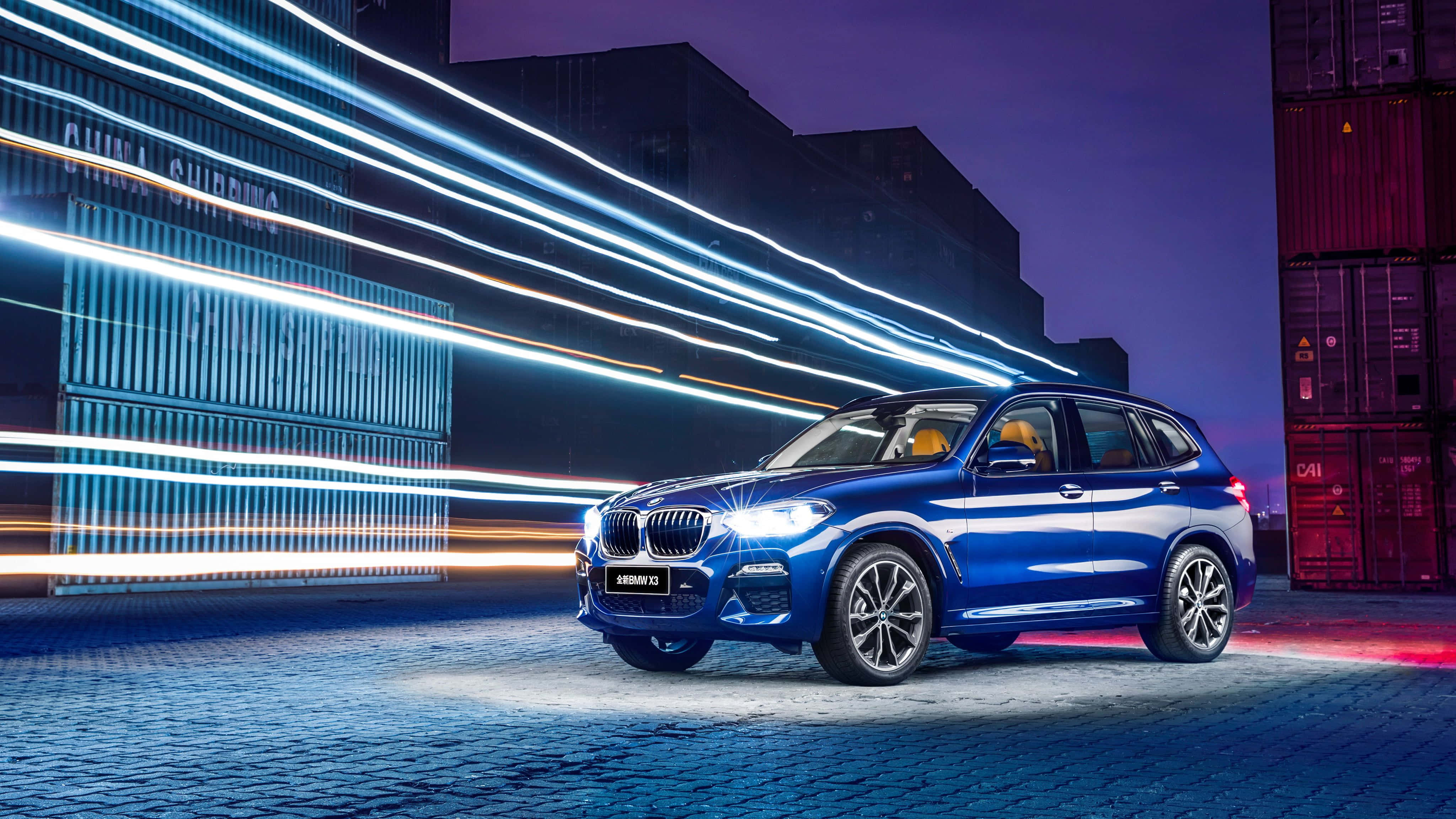 Bmw X3 桌布 壁紙 — 一輛充滿活力的藍色BMW X3 SUV在霓虹燈條下閃耀，背景是暮色城市中的貨運集裝箱。