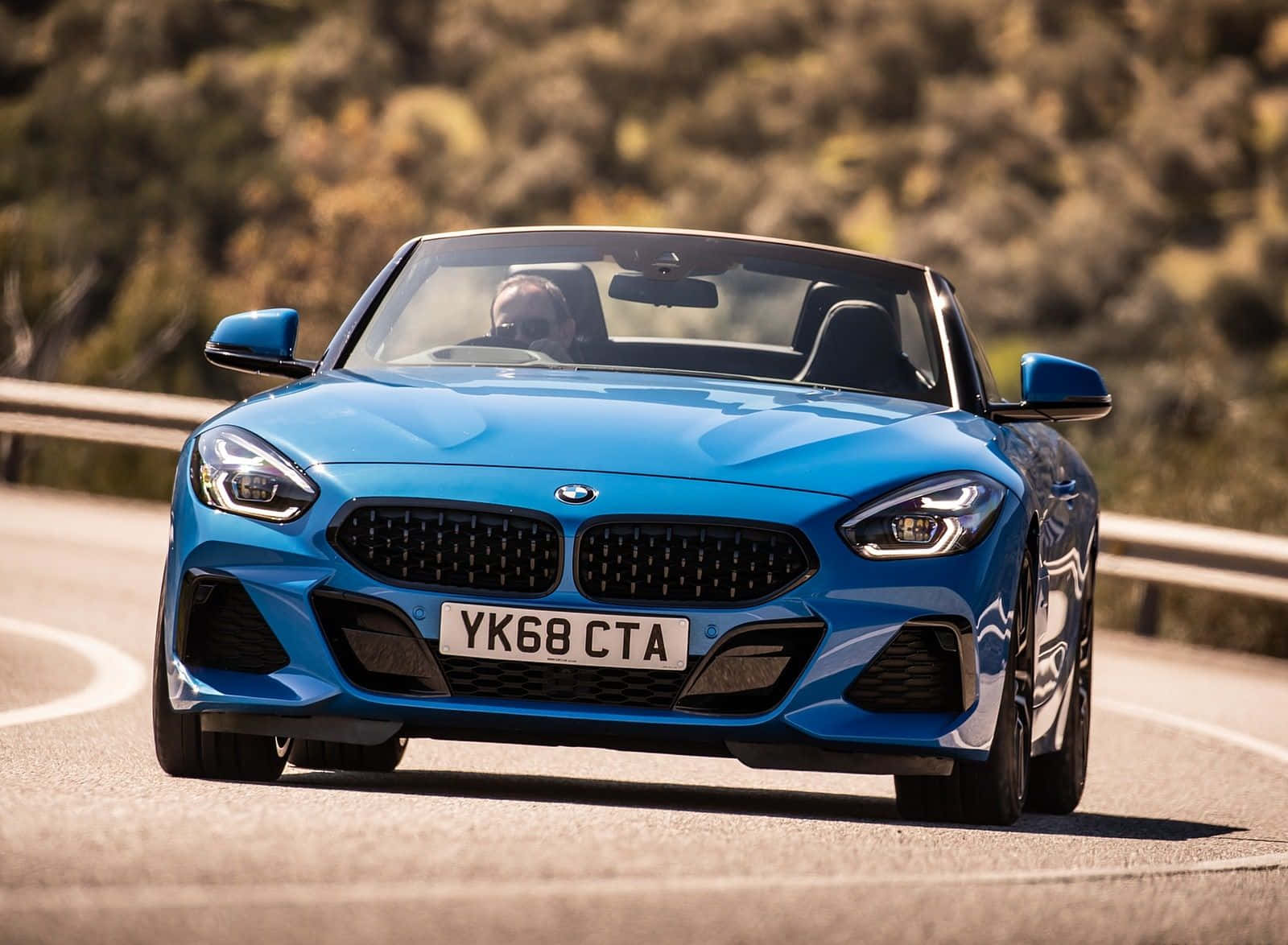 Bmw Z4 桌布 壁紙 — 一輛充滿活力的藍色BMW Z4開篷跑車在明亮的陽光下沿著蜿蜒的山路飛馳。