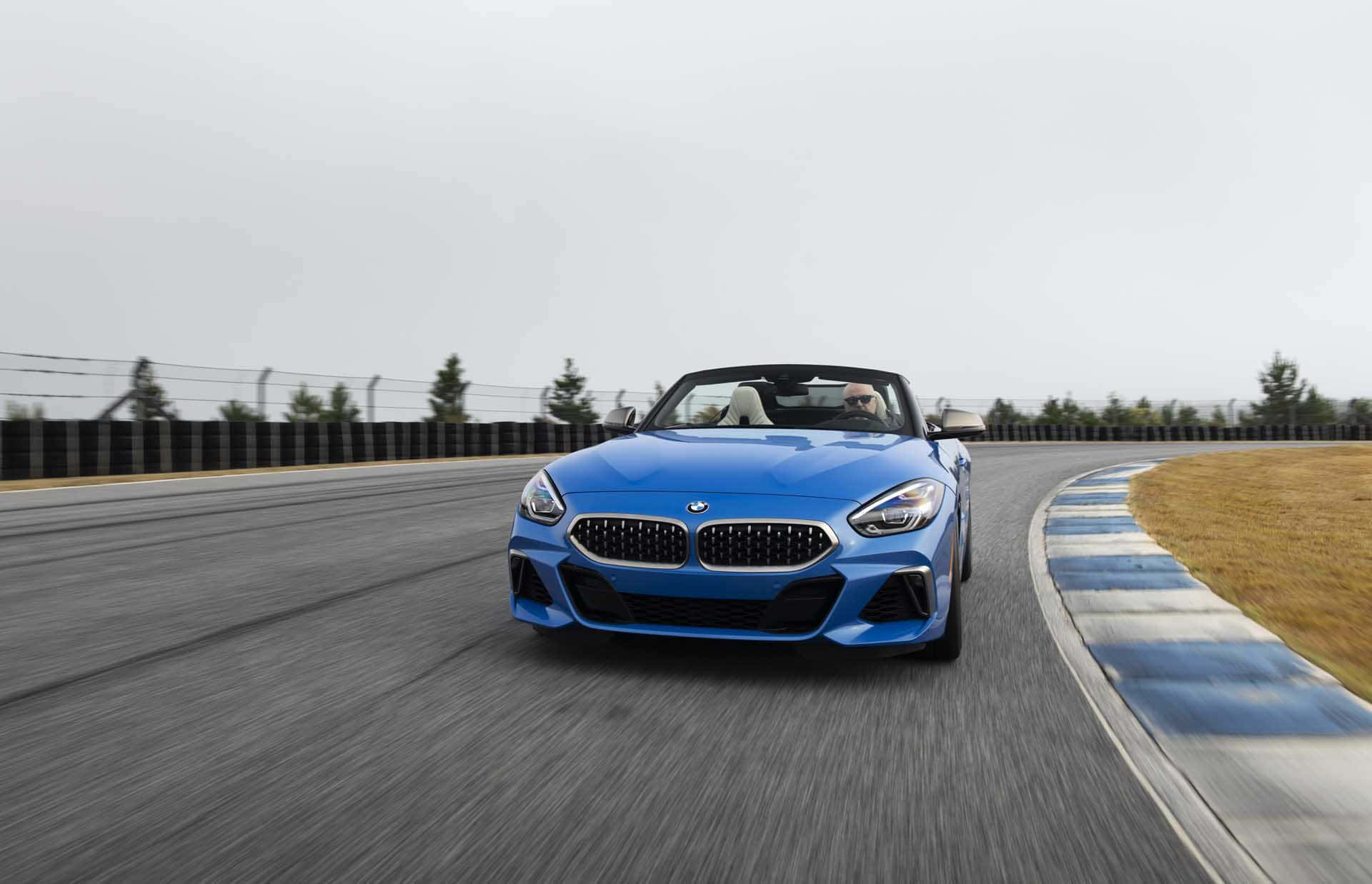 Bmw Z4 桌布 壁紙 — 一輛充滿活力的藍色BMW Z4開篷跑車在賽道上高速行駛，帶有動態模糊效果，司機手握方向盤。
