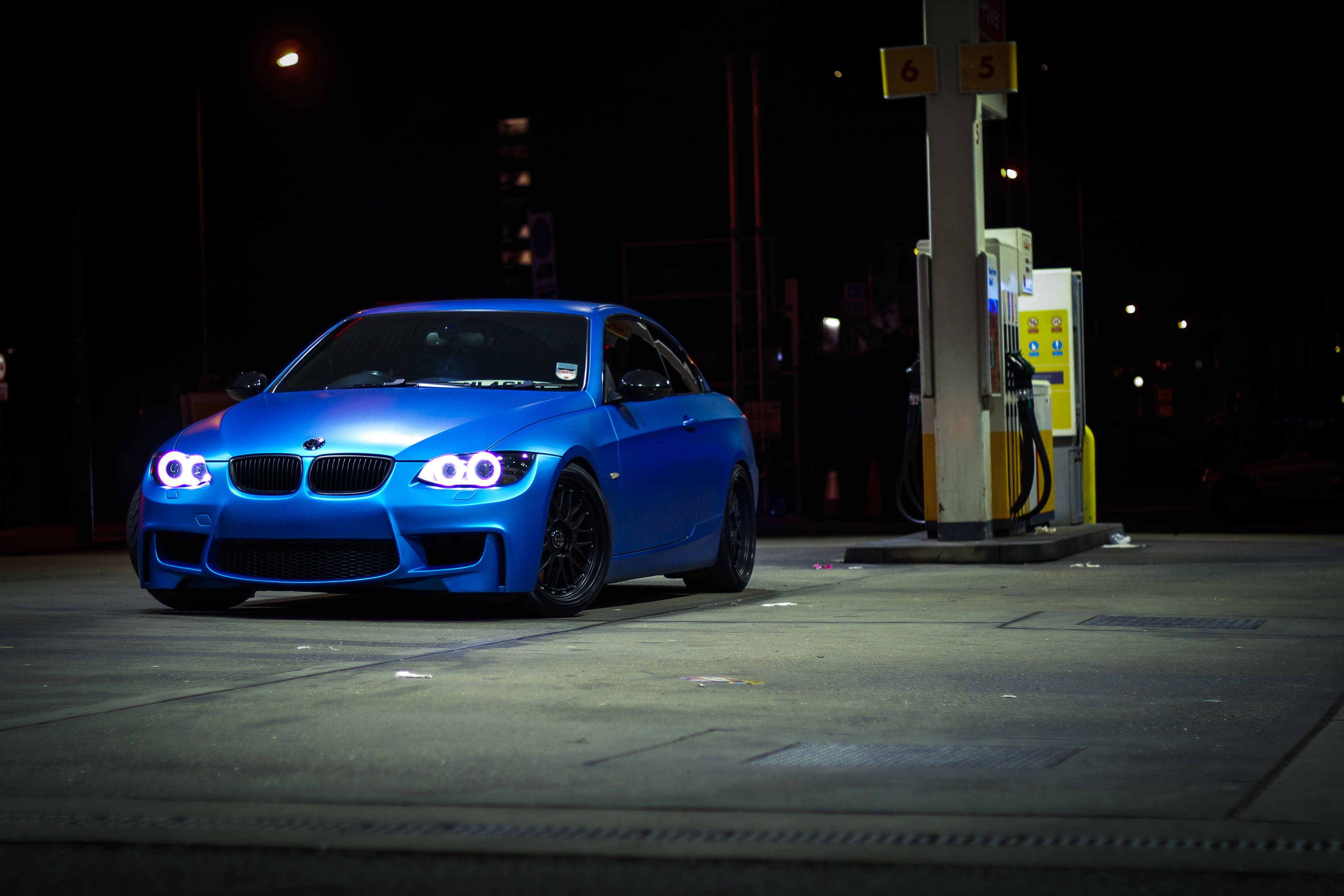 Bmw M4 桌布 壁紙 — 一輛充滿活力的藍色BMW跑車，車頭燈閃爍，夜間停在加油站。