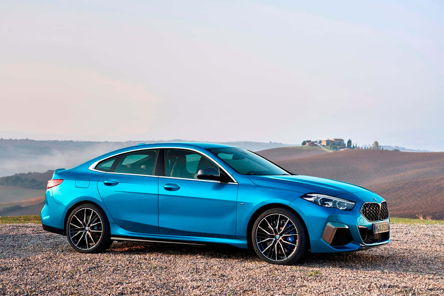 Bmw 2 Series 桌布 壁紙 — 一輛充滿活力的藍色BMW轎車停泊在碎石山坡上，俯瞰日出時霧氣繚繞的連綿山丘。