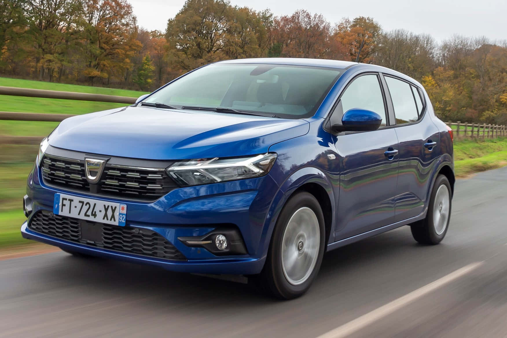 Dacia 桌布 壁紙 — 一輛充滿活力的藍色Dacia Sandero掀背車在鄉村道路上疾馳，背景是秋天的樹木。
