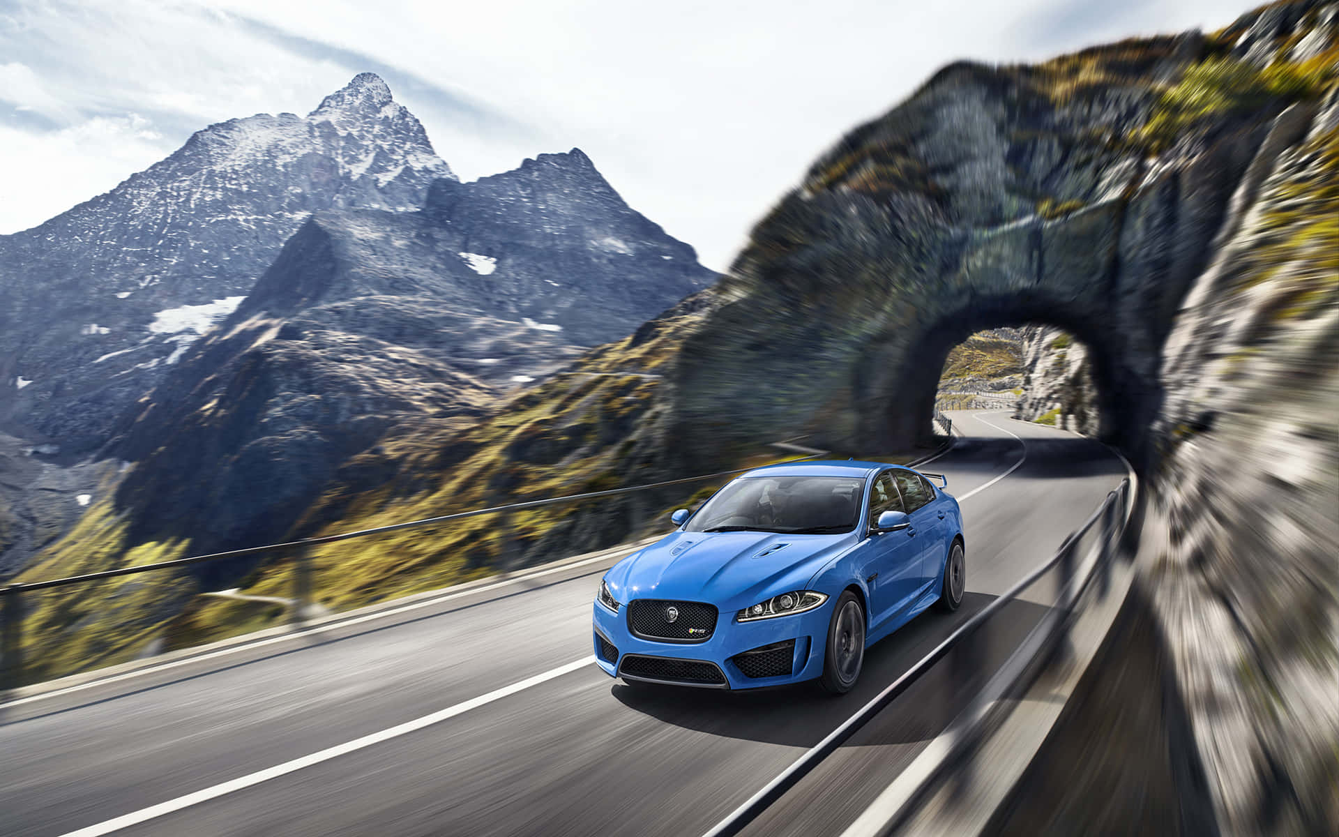 Jaguar Xfr 桌布 壁紙 — 一輛充滿活力的藍色Jaguar F-Type在雪山峰和綠色山坡背景中疾速穿過山間隧道。