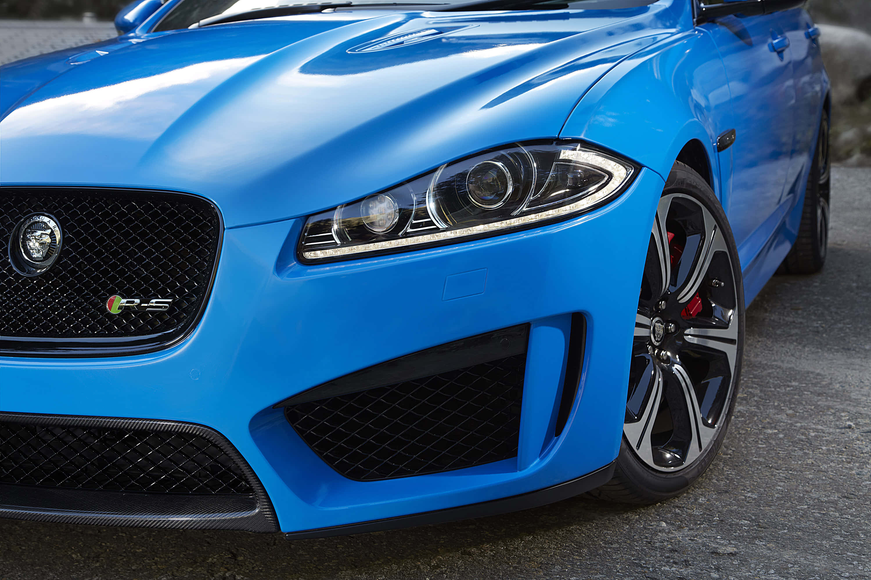 Jaguar Xfr 桌布 壁紙 — 一輛充滿活力的藍色Jaguar F-Type RS跑車在日光下閃耀，帶有侵略性的前格柵和碳纖維飾件。