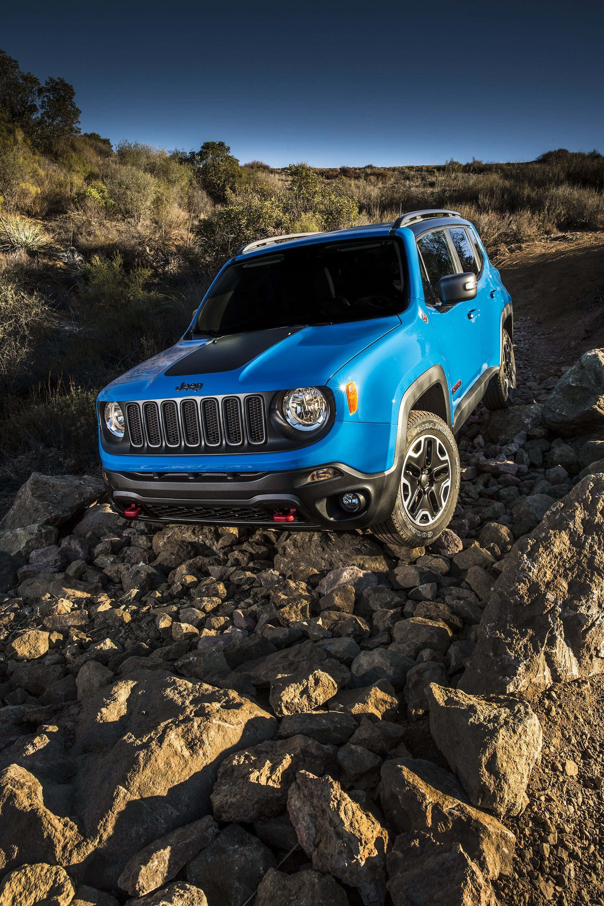 Jeep Renegade 桌布 壁紙 — 一輛充滿活力的藍色Jeep Renegade在晴朗的藍天下行駛在崎嶇的岩石小徑上，背景有乾燥的灌木叢。