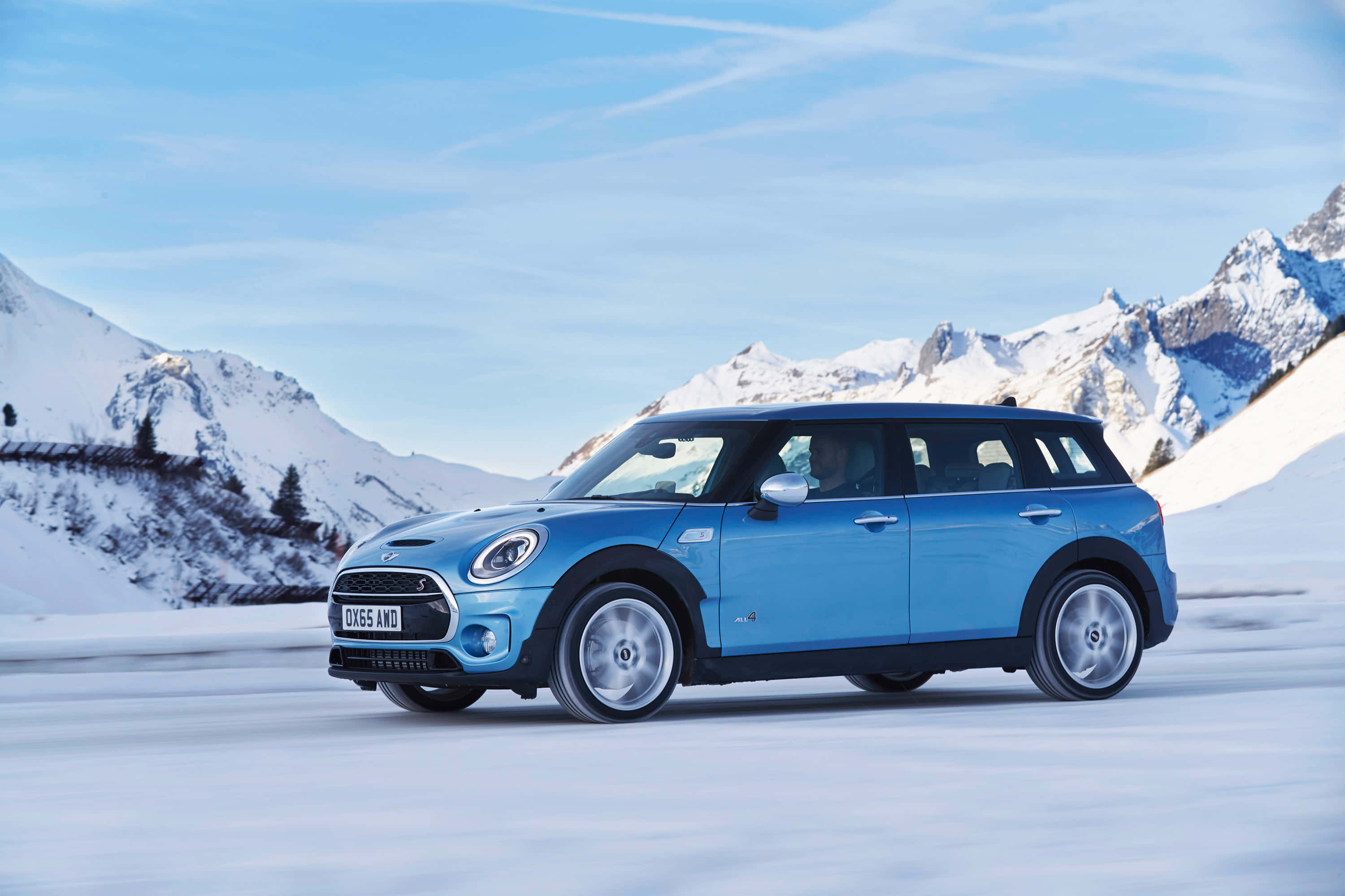 Mini Cooper S Clubman All4 桌布 壁紙 — 一輛充滿活力的藍色MINI Countryman在晴朗的藍天下，行駛在白雪覆蓋的山路上，背景是白雪皚皚的山峰。