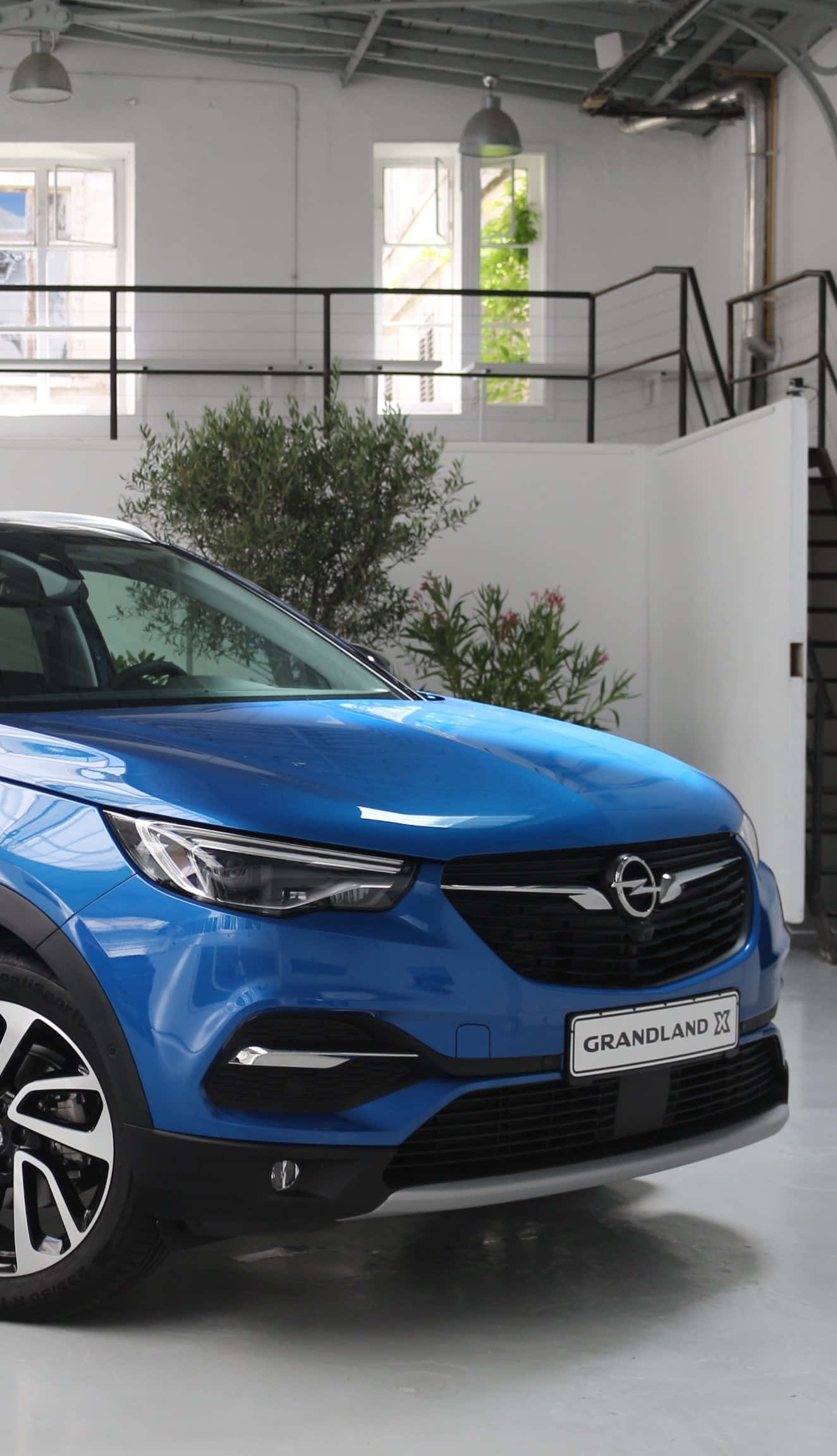 Opel Grandland X 桌布 壁紙 — 一輛充滿活力的藍色Opel Grandland X SUV在明亮的工業風格展廳中展示，配有白色牆壁和綠色植物。