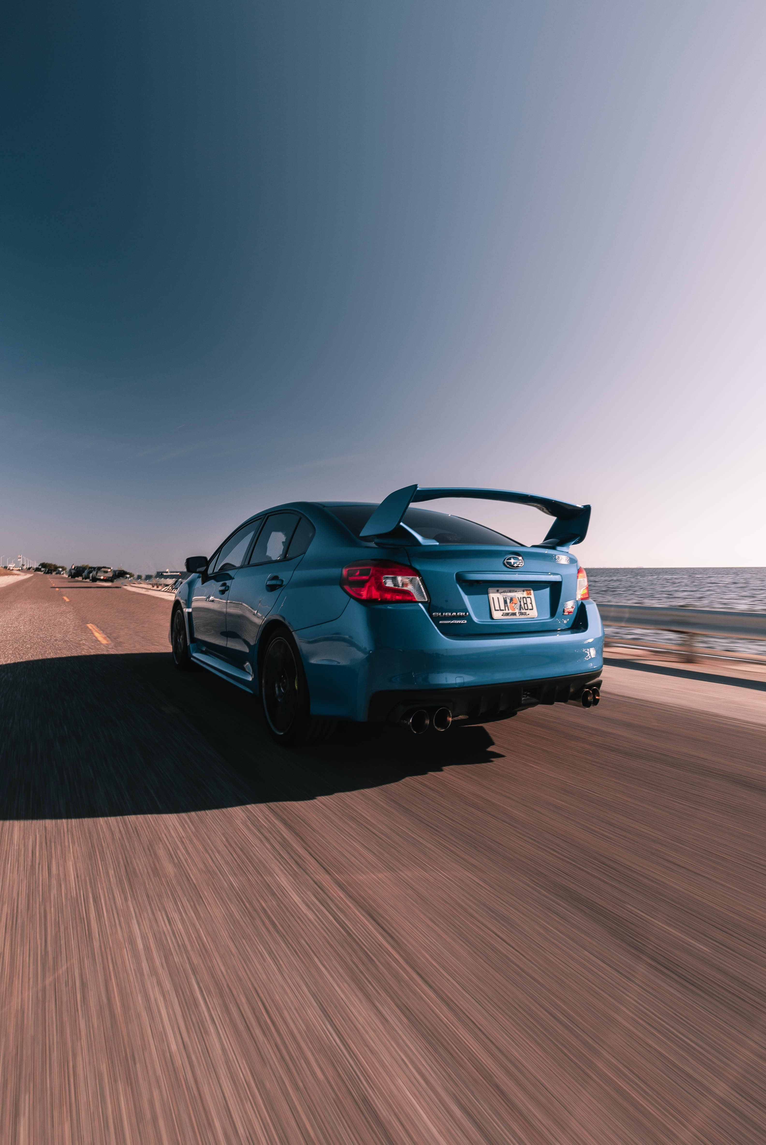 speeding car 桌布 壁紙 — 一輛充滿活力的藍色Subaru WRX STI在晴朗的天空下沿著海岸高速公路奔馳，帶有動態模糊效果。