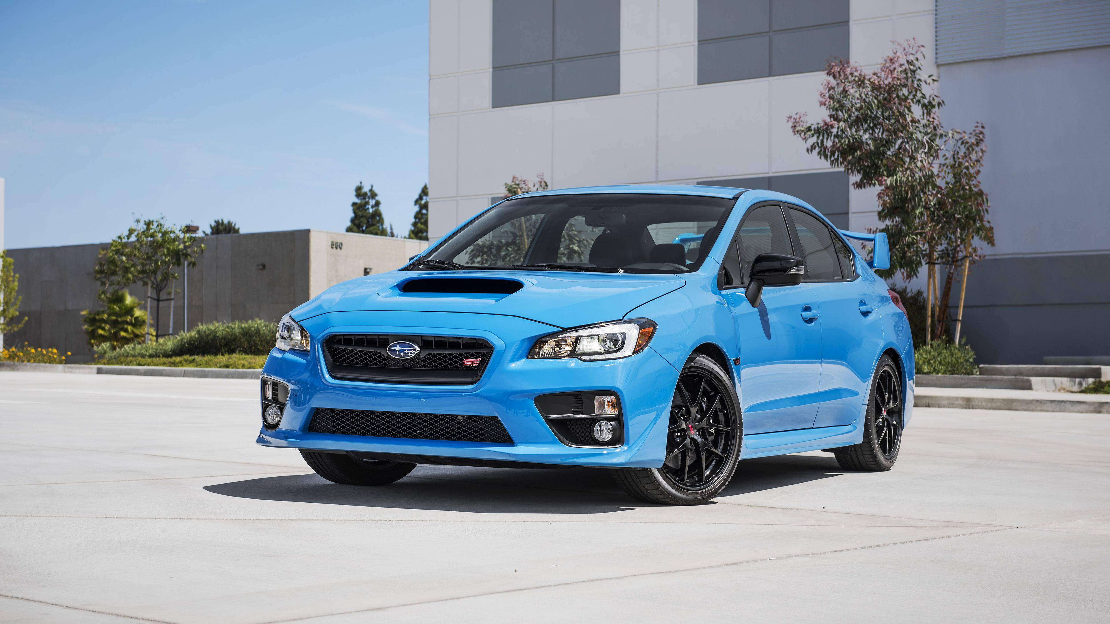 Sports Car 桌布 壁紙 — 一輛充滿活力的藍色Subaru WRX STI跑車停放在混凝土停車場上，天空清澈湛藍，背景是現代建築。