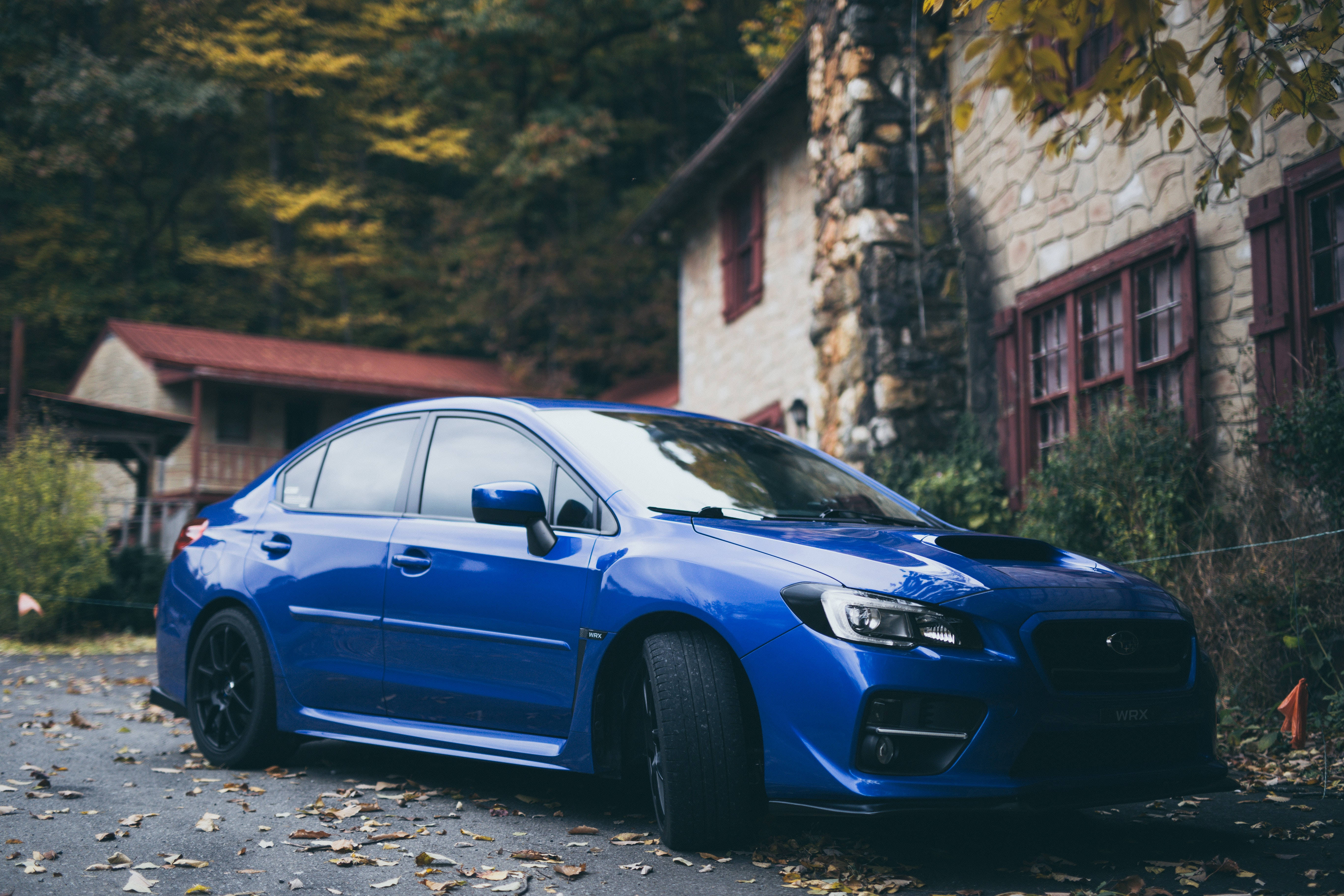 subaru 桌布 壁紙 — 一輛充滿活力的藍色Subaru WRX STI停泊在落葉滿佈的車道上，旁邊是一座質樸的石屋，正值秋季。