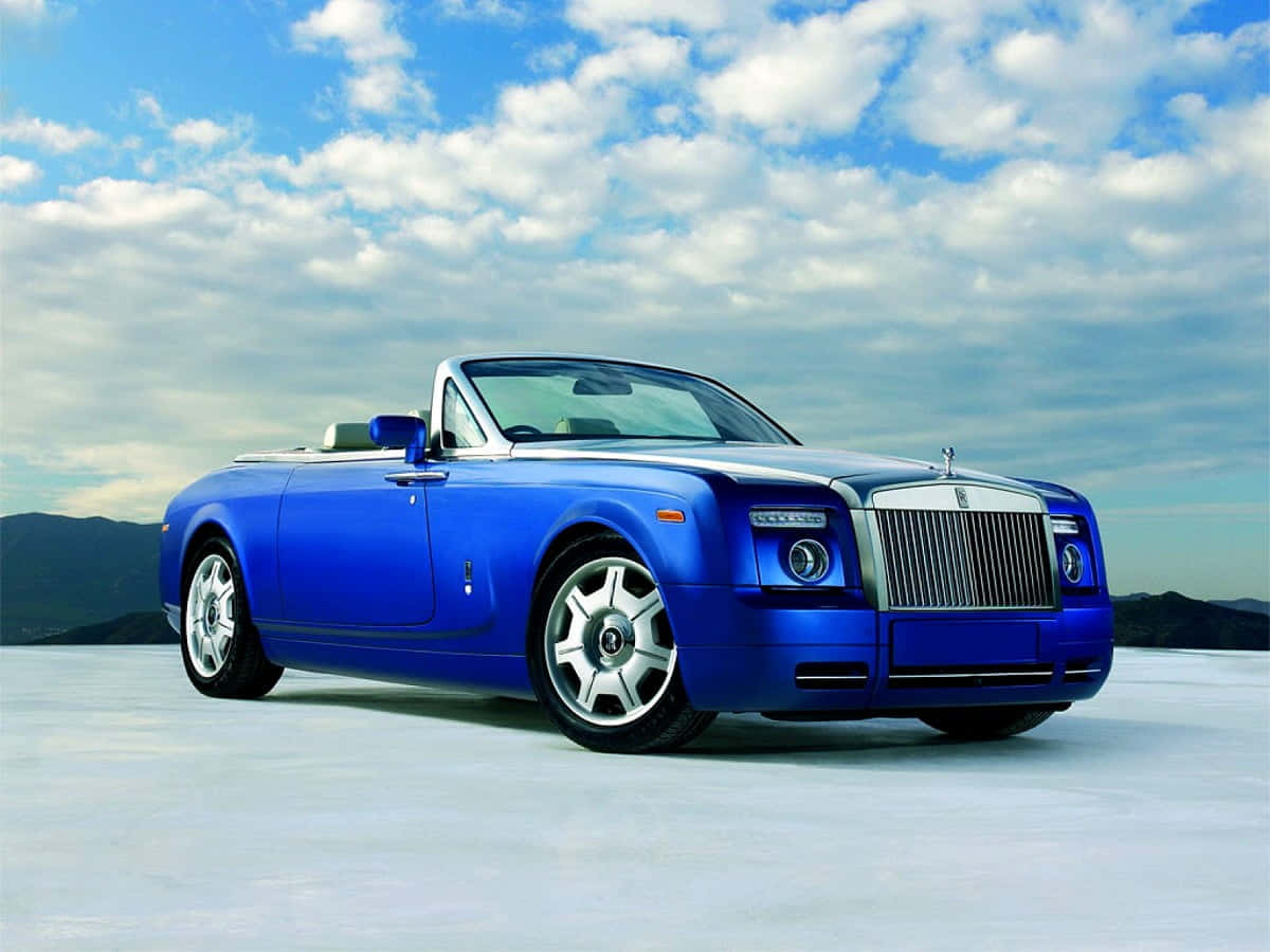 Rolls Royce 桌布 壁紙 — 一輛充滿活力的藍色勞斯萊斯幻影敞篷轎跑車在晴朗的天空下閃閃發光，天空中有蓬鬆的雲朵和遠山。