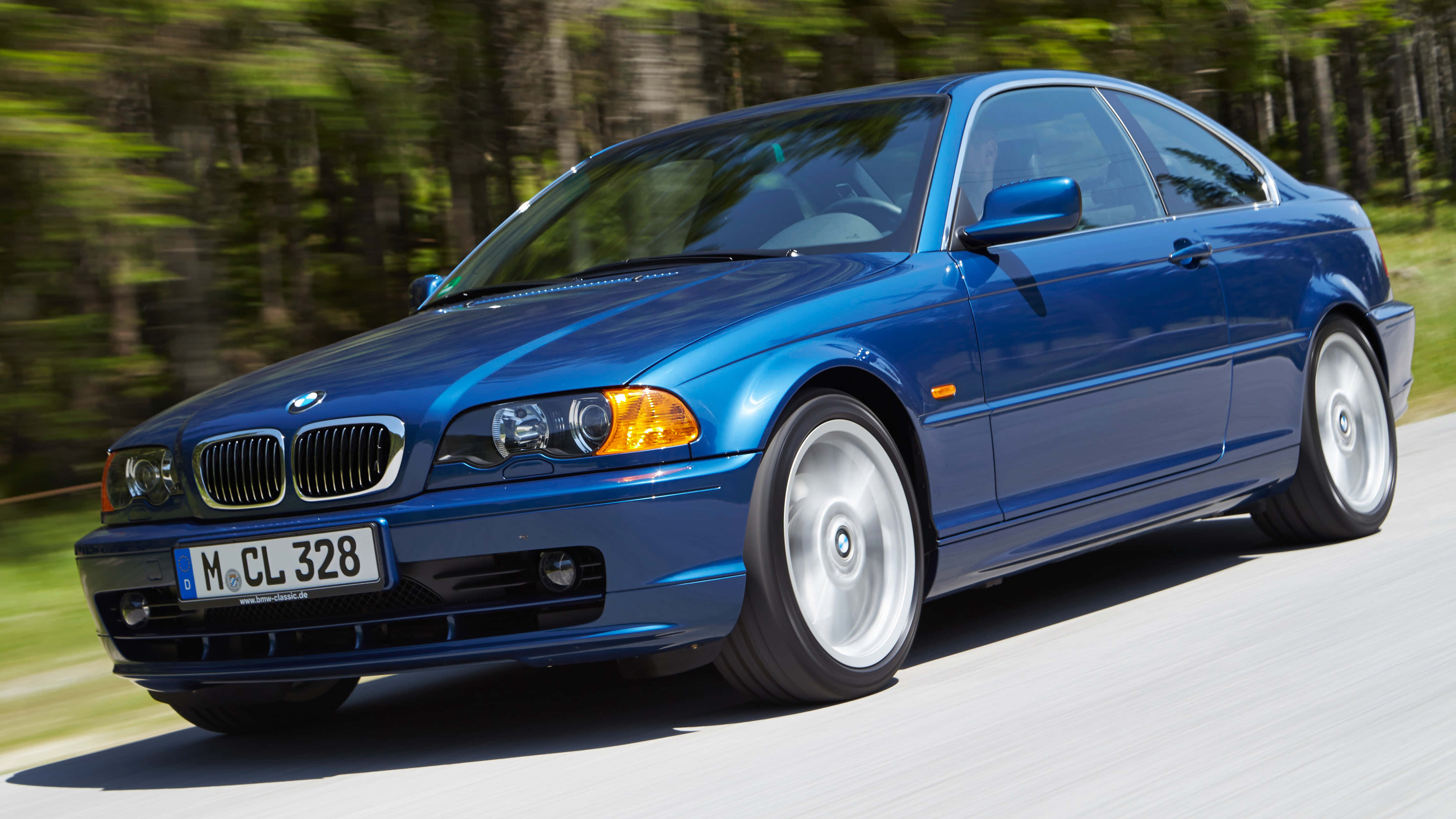 Bmw 3 Series 桌布 壁紙 — 一輛充滿活力的藍色寶馬3系雙門轎跑車在森林道路上行駛，動態模糊傳達出動感。