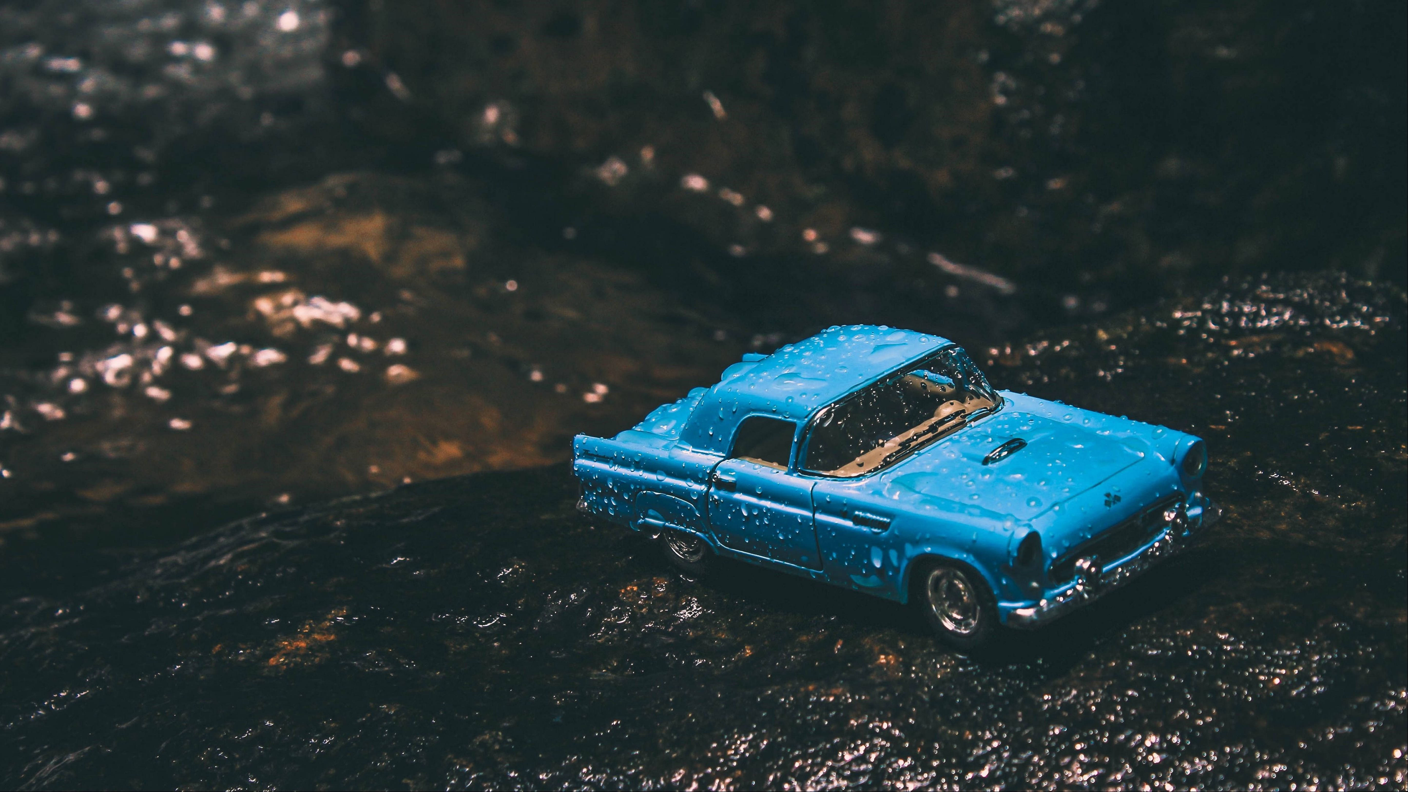 Retro 桌布 壁紙 — 一輛充滿活力的藍色復古玩具車停在濕潤的深色岩石上，旁邊是閃閃發光的小溪，在柔和自然光下。