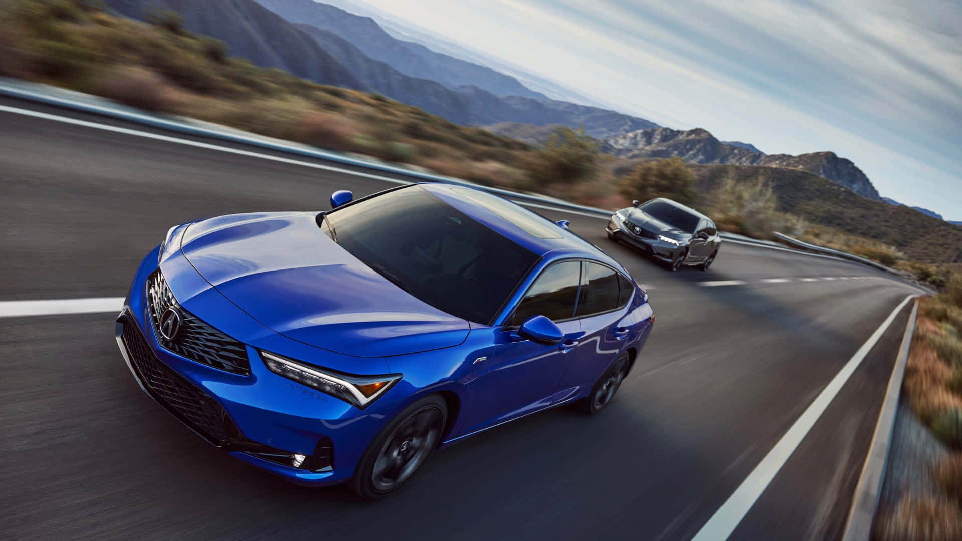 Acura Integra 桌布 壁紙 — 一輛充滿活力的藍色房車在晴朗的天空下沿著蜿蜒的山路疾馳，後面跟著一輛銀色汽車。