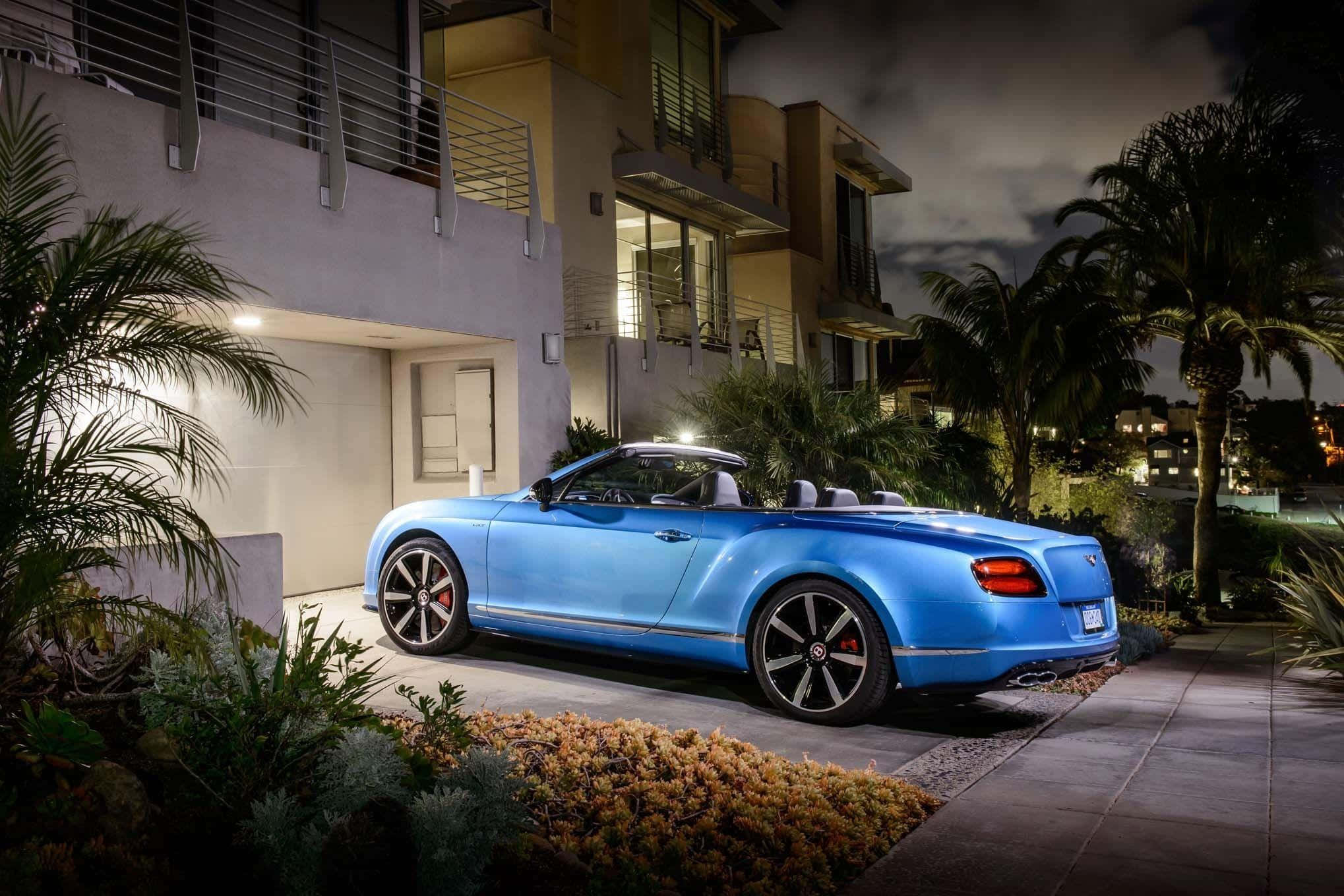 Convertible 桌布 壁紙 — 一輛充滿活力的藍色敞篷跑車在夜間停在一棟有棕櫚樹和溫暖照明的現代房屋前。