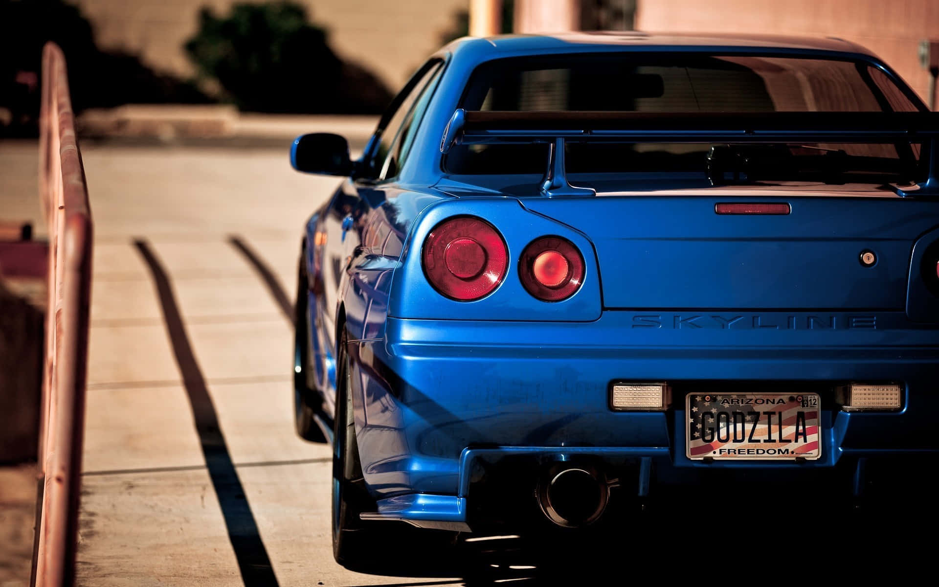 Gtr 桌布 壁紙 — 一輛充滿活力的藍色日產Skyline R34跑車停泊在陽光普照的行人路上，帶有Godzilla車牌。