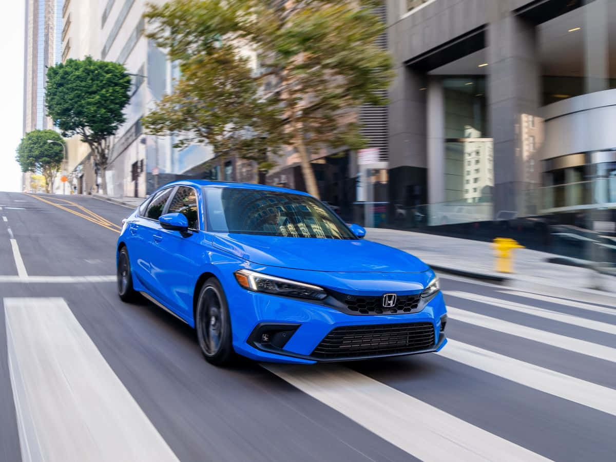 Honda Civic 桌布 壁紙 — 一輛充滿活力的藍色本田房車在城市的街道上飛馳，路面呈現動態模糊，背景是現代建築。