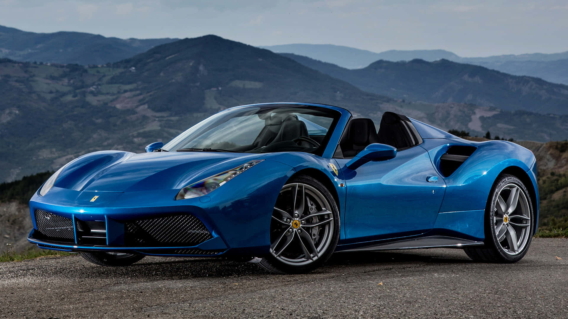 Ferrari 488 Spider 桌布 壁紙 — 一輛充滿活力的藍色法拉利488 Spider敞篷車停在山路上，背景是起伏的丘陵。