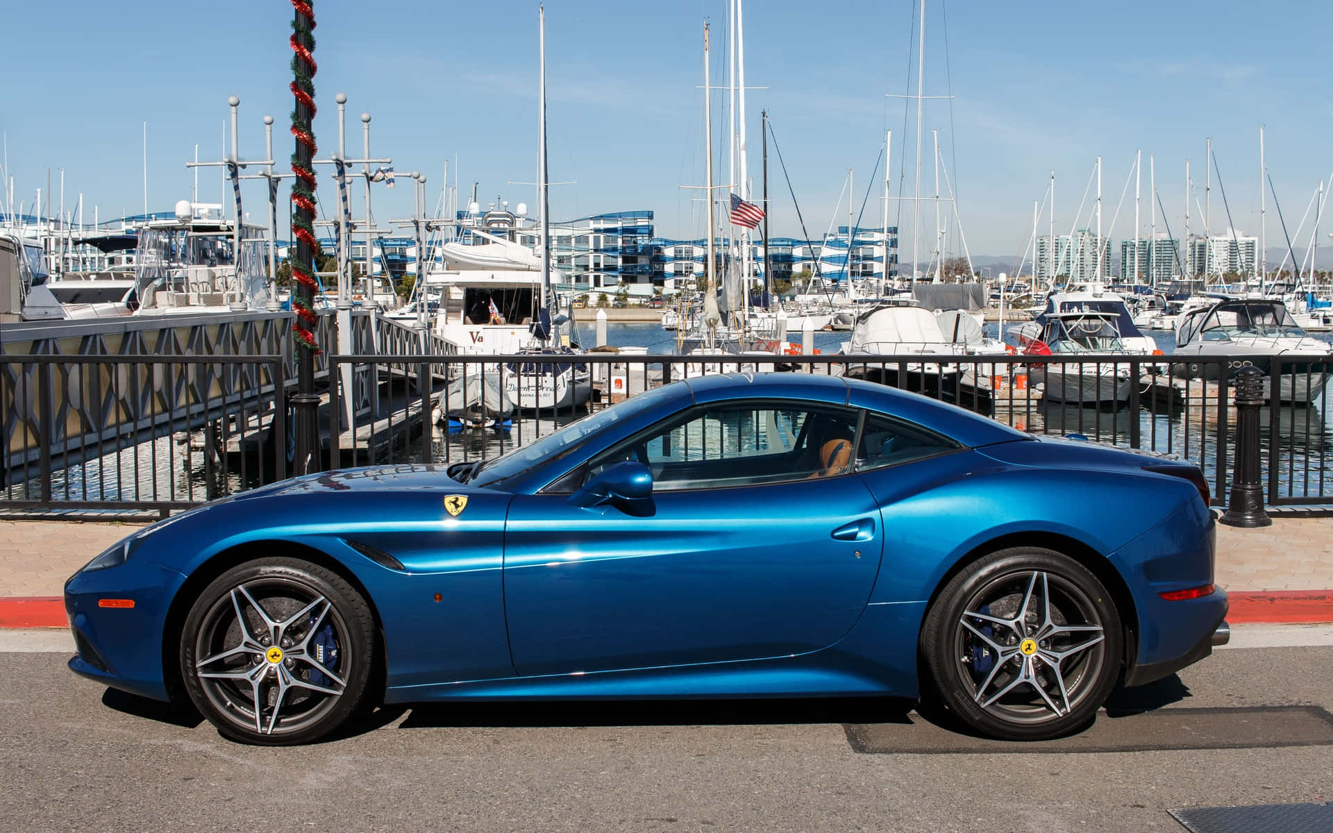 Ferrari California T 桌布 壁紙 — 一輛充滿活力的藍色法拉利跑車停泊在一個充滿遊艇的碼頭旁，天空清澈湛藍。