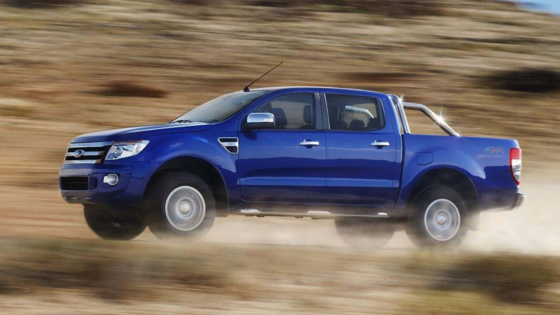 Ford Ranger 桌布 壁紙 — 一輛充滿活力的藍色皮卡車在塵土飛揚的地形上疾馳，揚起灰塵，形成動態模糊。