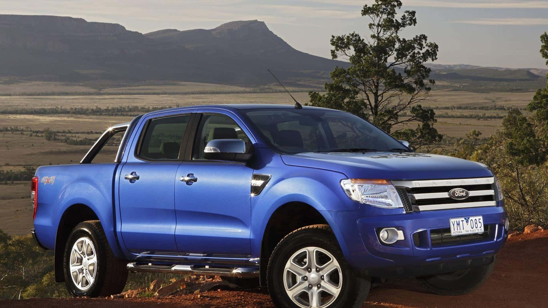 Ford Ranger 桌布 壁紙 — 一輛充滿活力的藍色福特 Ranger 皮卡車停在一條泥路上，背景是崎嶇的山脈和稀疏的樹木，天空晴朗。