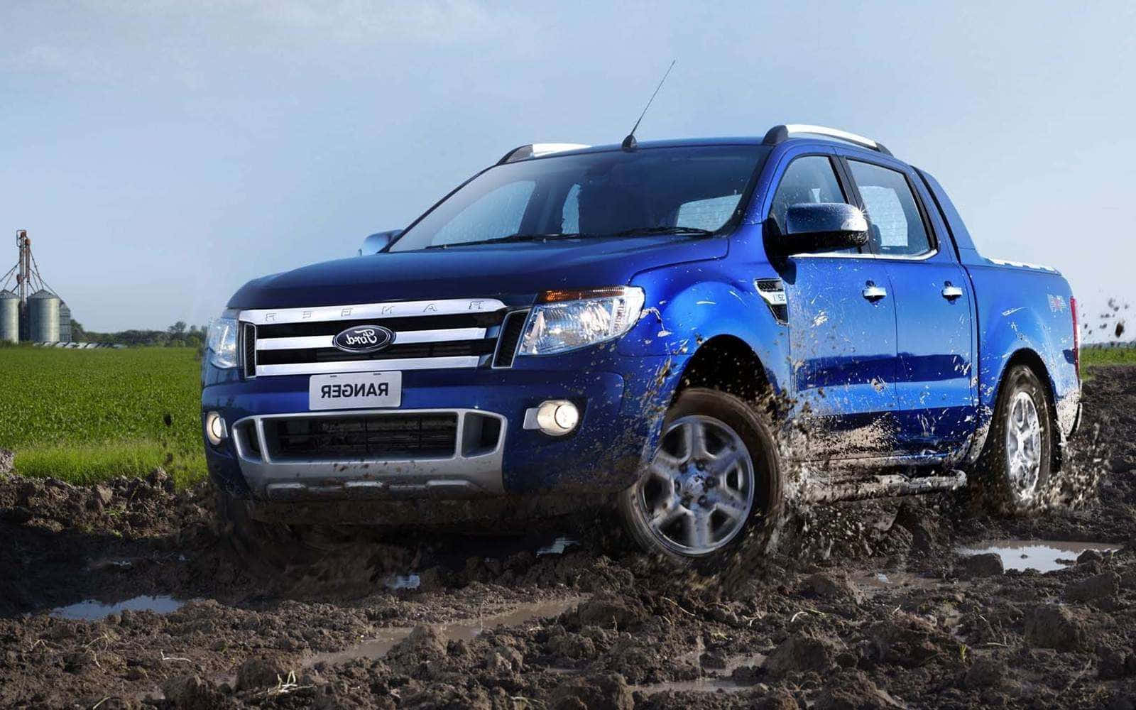 Ford Ranger 桌布 壁紙 — 一輛充滿活力的藍色福特 Ranger 皮卡車在深泥濘的地形中強勁行駛，泥漿飛濺，背景是鄉村風光，有綠色田野和筒倉，天空晴朗。